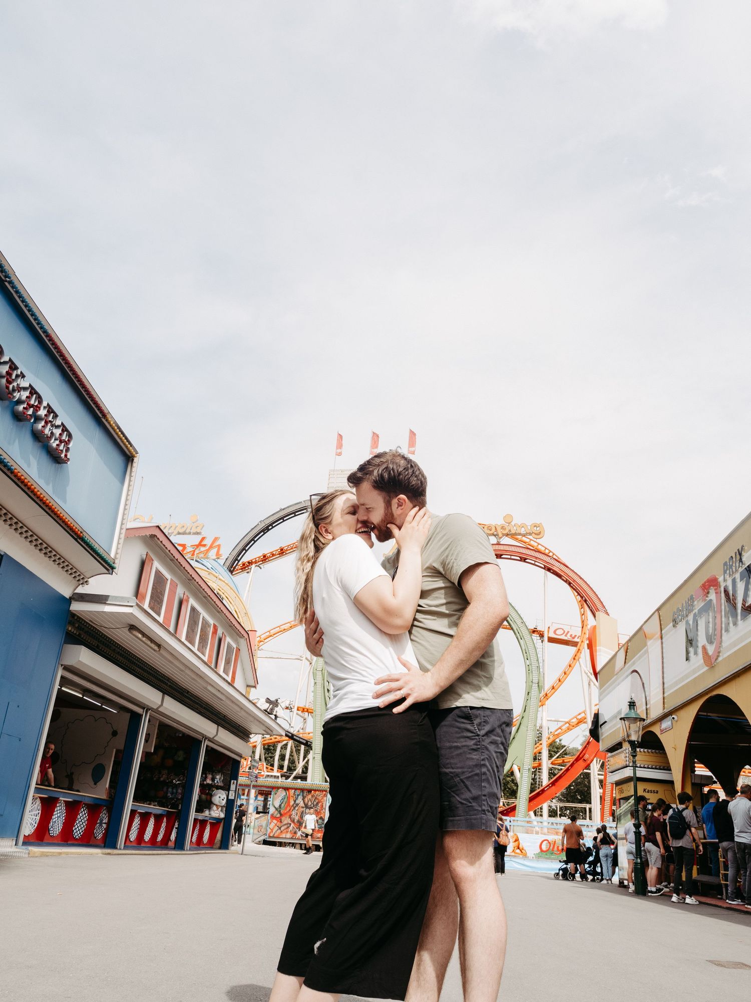 Romantic moment between couple at carnival with rides and attractions in background.