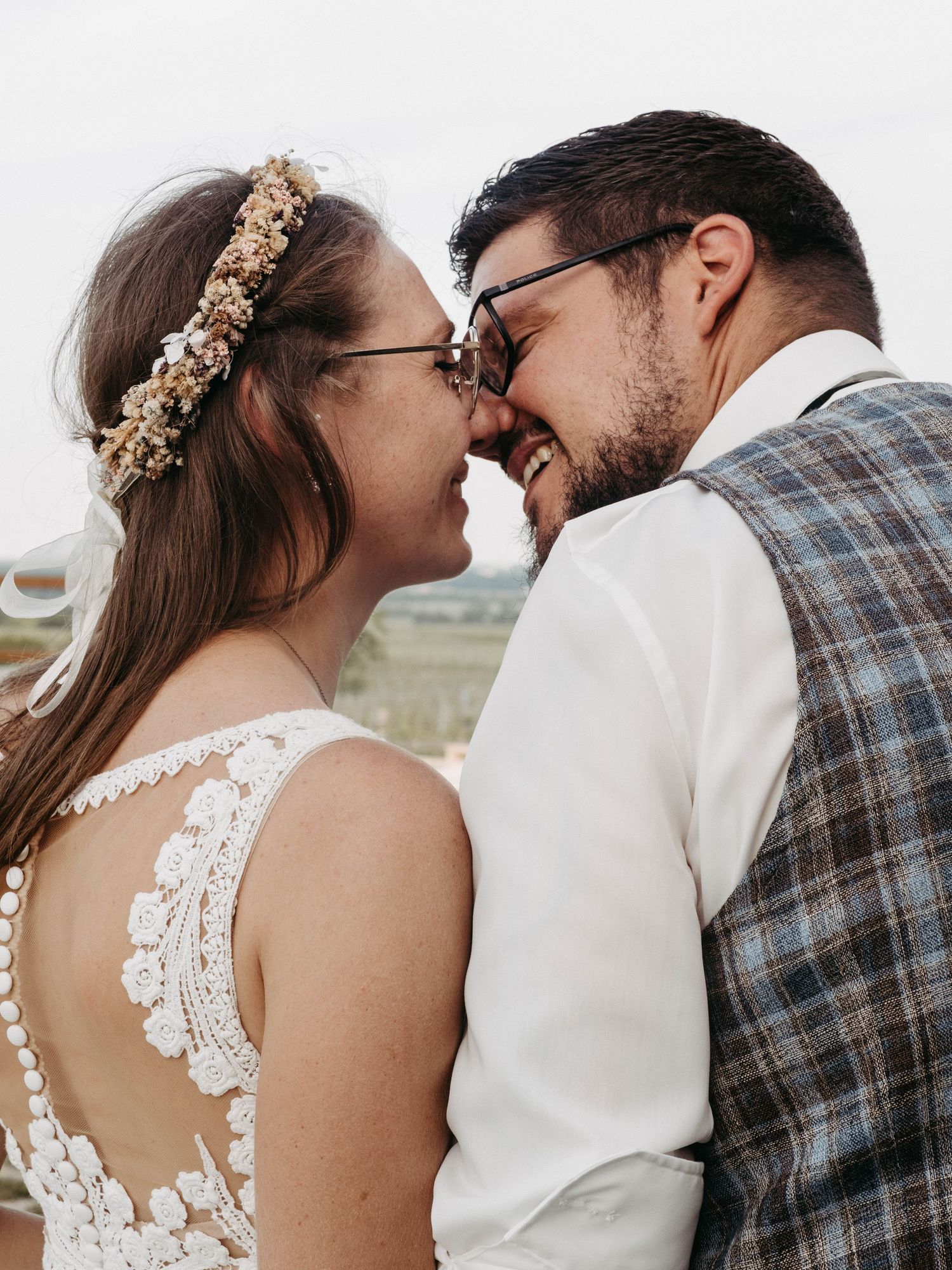 A joyful bride and groom share an intimate moment, touching foreheads and smiling on their wedding day outdoors.