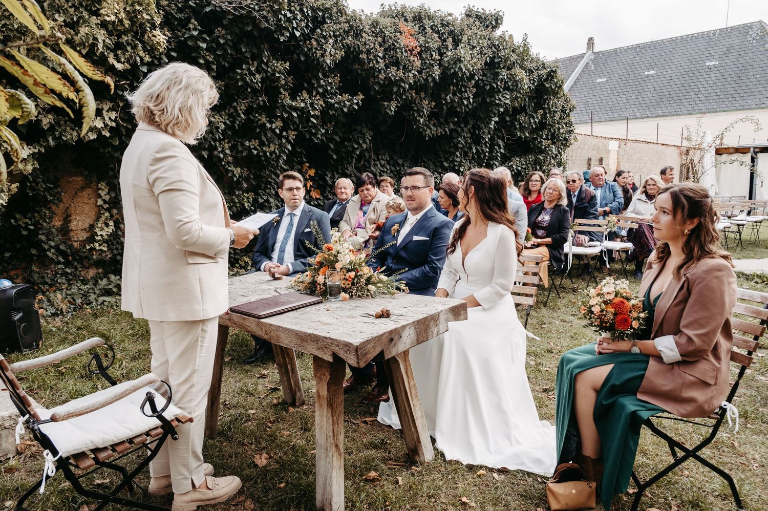 Outdoor wedding ceremony with couple at rustic wooden table and seated guests.
