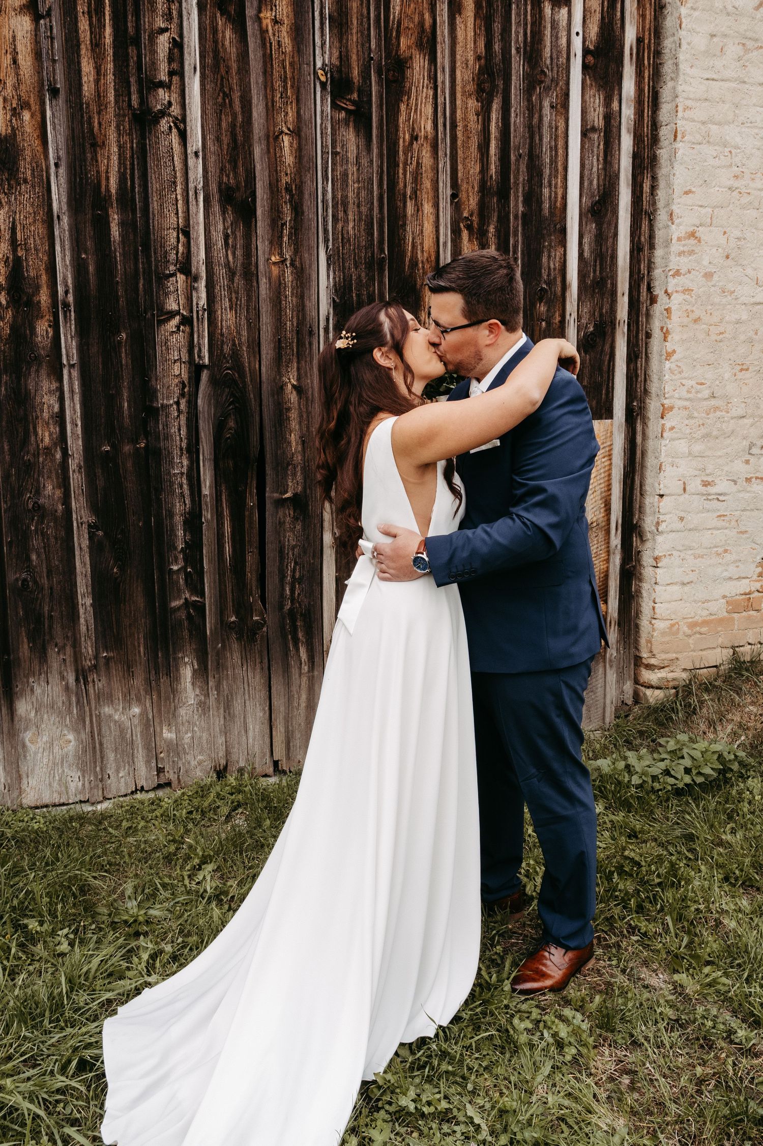 Bride and groom sharing romantic kiss in front of rustic wooden barn wall.