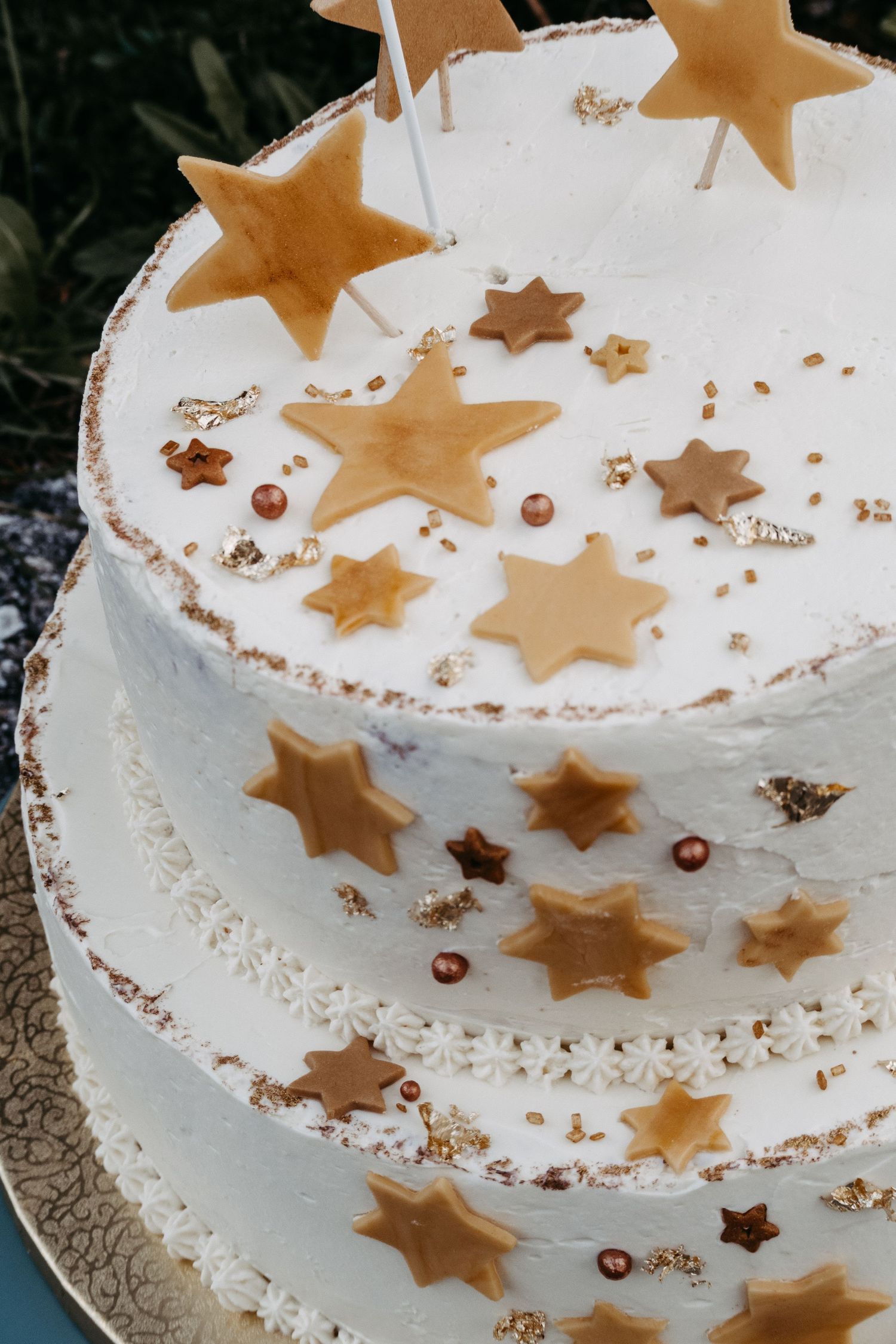 Elegant two-tier white wedding cake decorated with golden star shapes, pearl beads, and gold leaf accents.