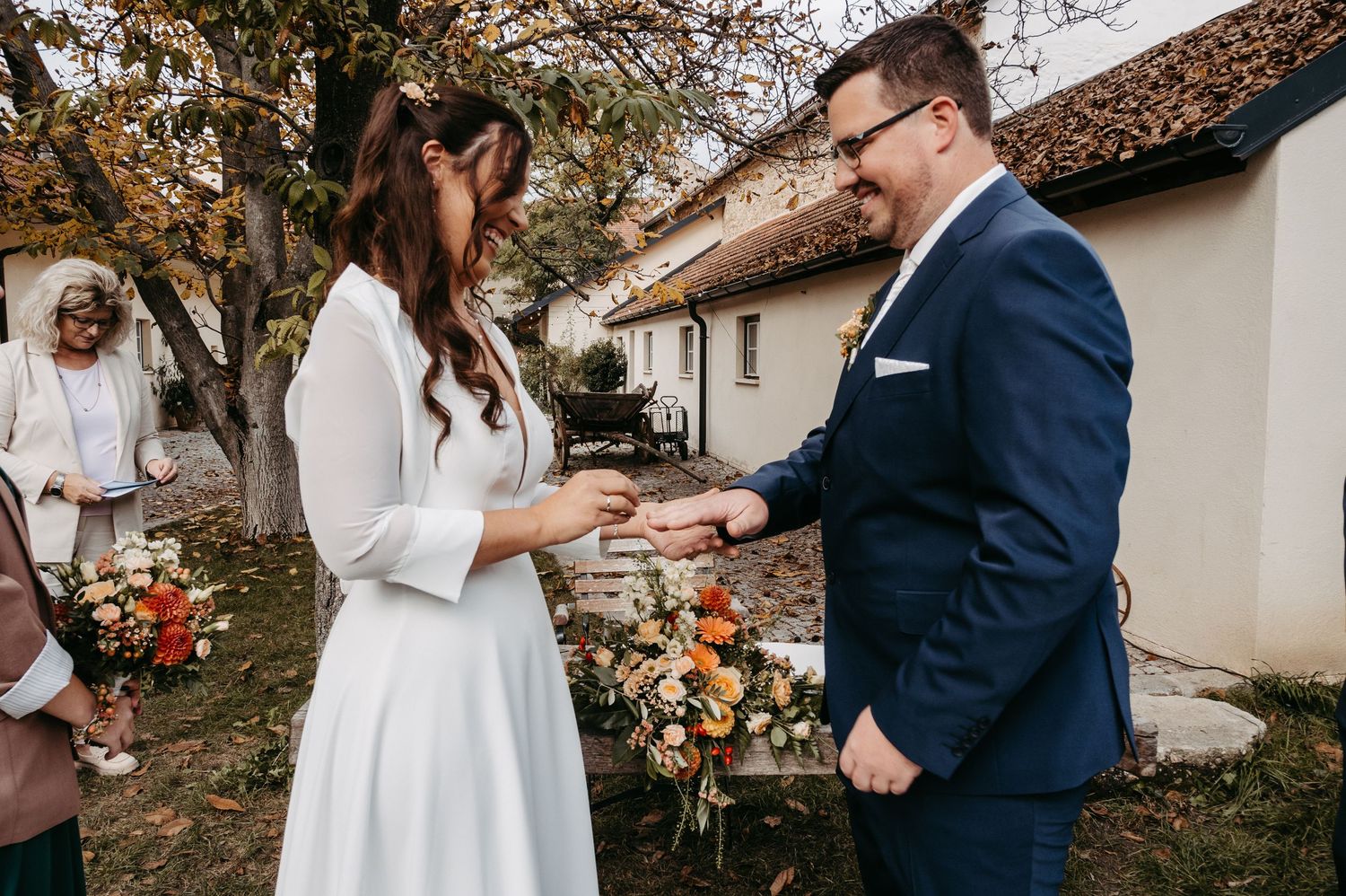 Bride and groom exchanging rings outdoors during intimate autumn wedding ceremony with floral bouquet.