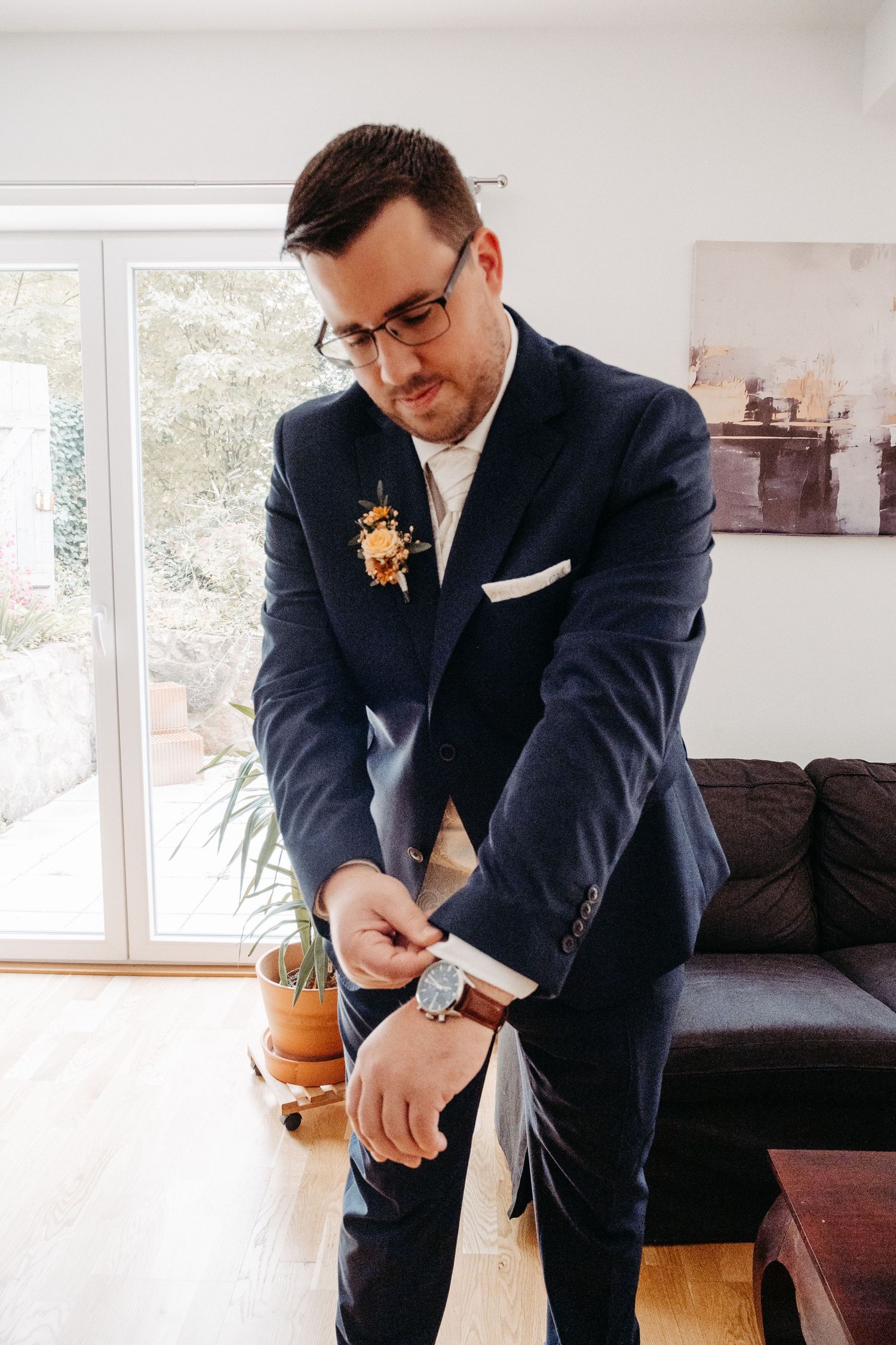 Groom in navy suit adjusting cufflinks before wedding ceremony.