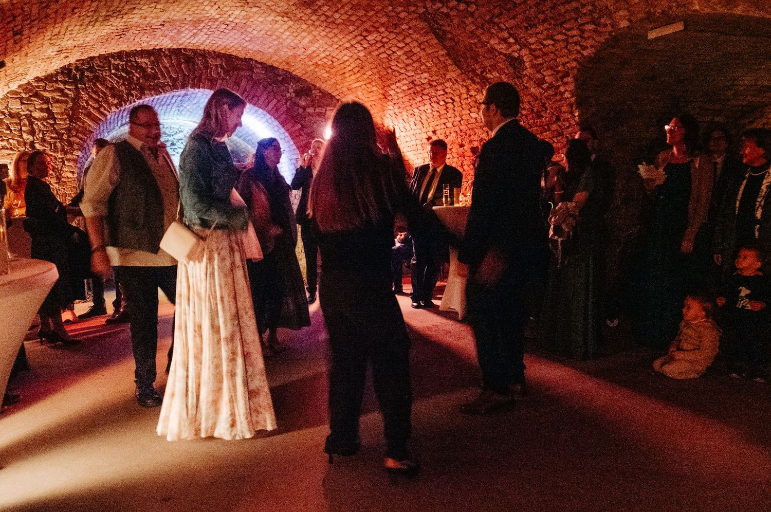 Wedding guests socializing in warmly lit vaulted stone cellar reception venue.