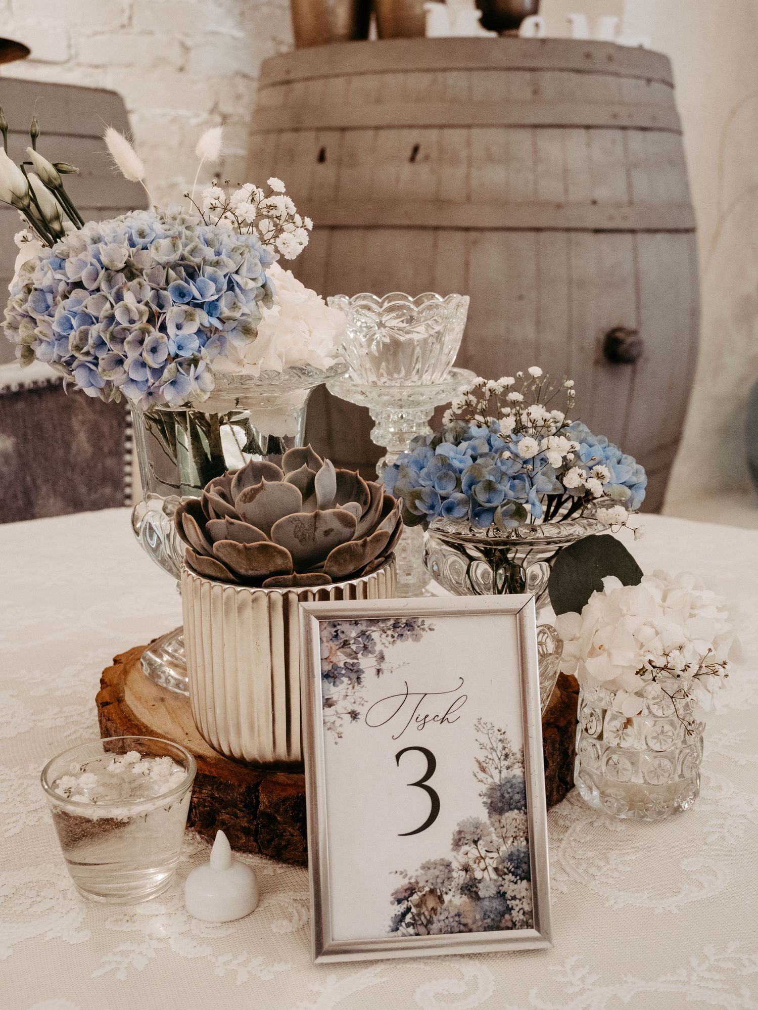 Elegant wedding table centerpiece with blue hydrangeas, succulents, and a framed table number 3 sign on a white linen.