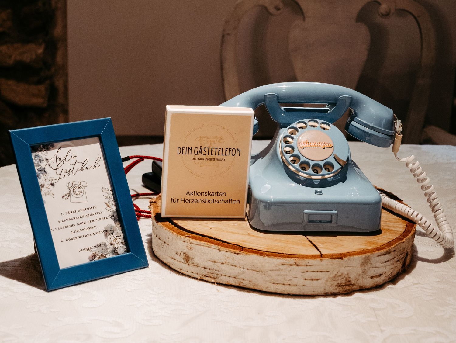 Vintage blue rotary phone on wooden slice beside a framed sign and guest book cards at a wedding reception.