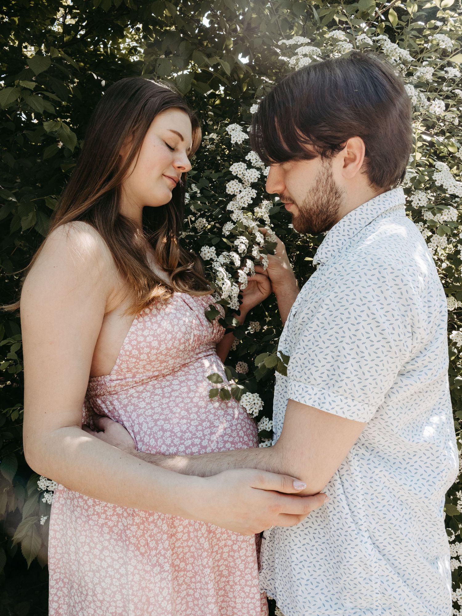 Couple sharing intimate moment in garden with blooming white flowers behind them.