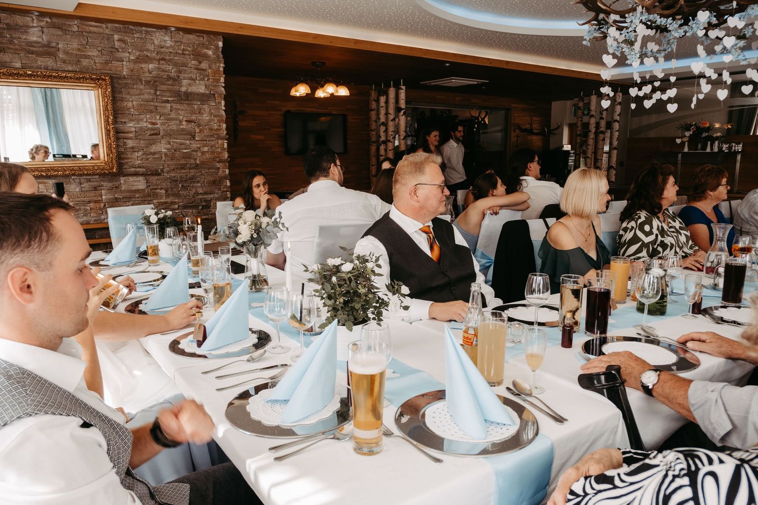Elegant wedding reception with guests seated at round tables adorned with blue napkins and floral centerpieces.