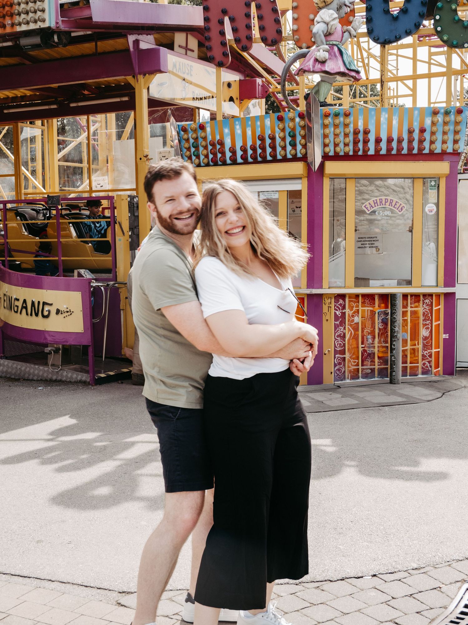 Happy couple posing playfully at colorful carnival amusement park.