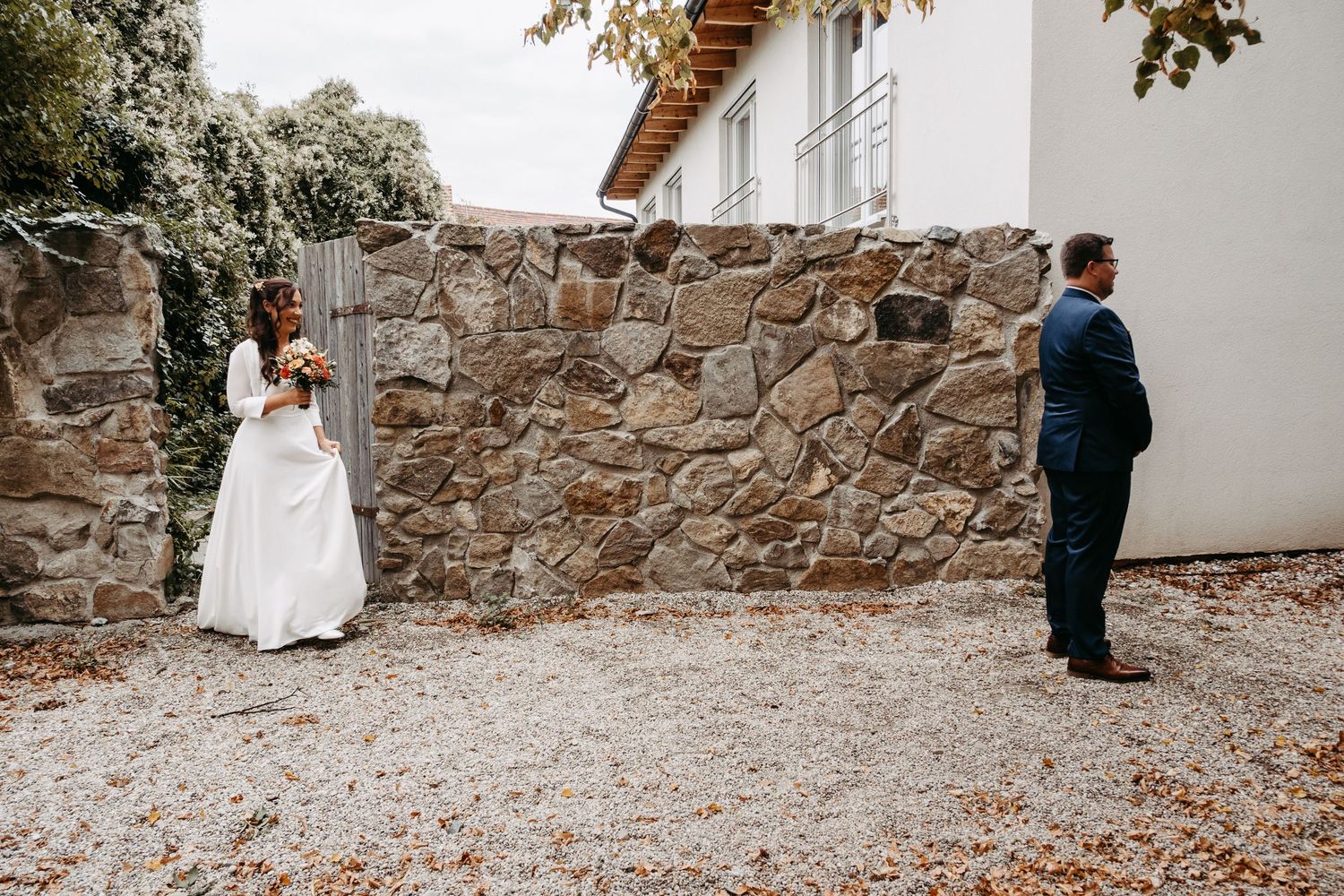 Bride and groom share first look moment by rustic stone wall outdoors.