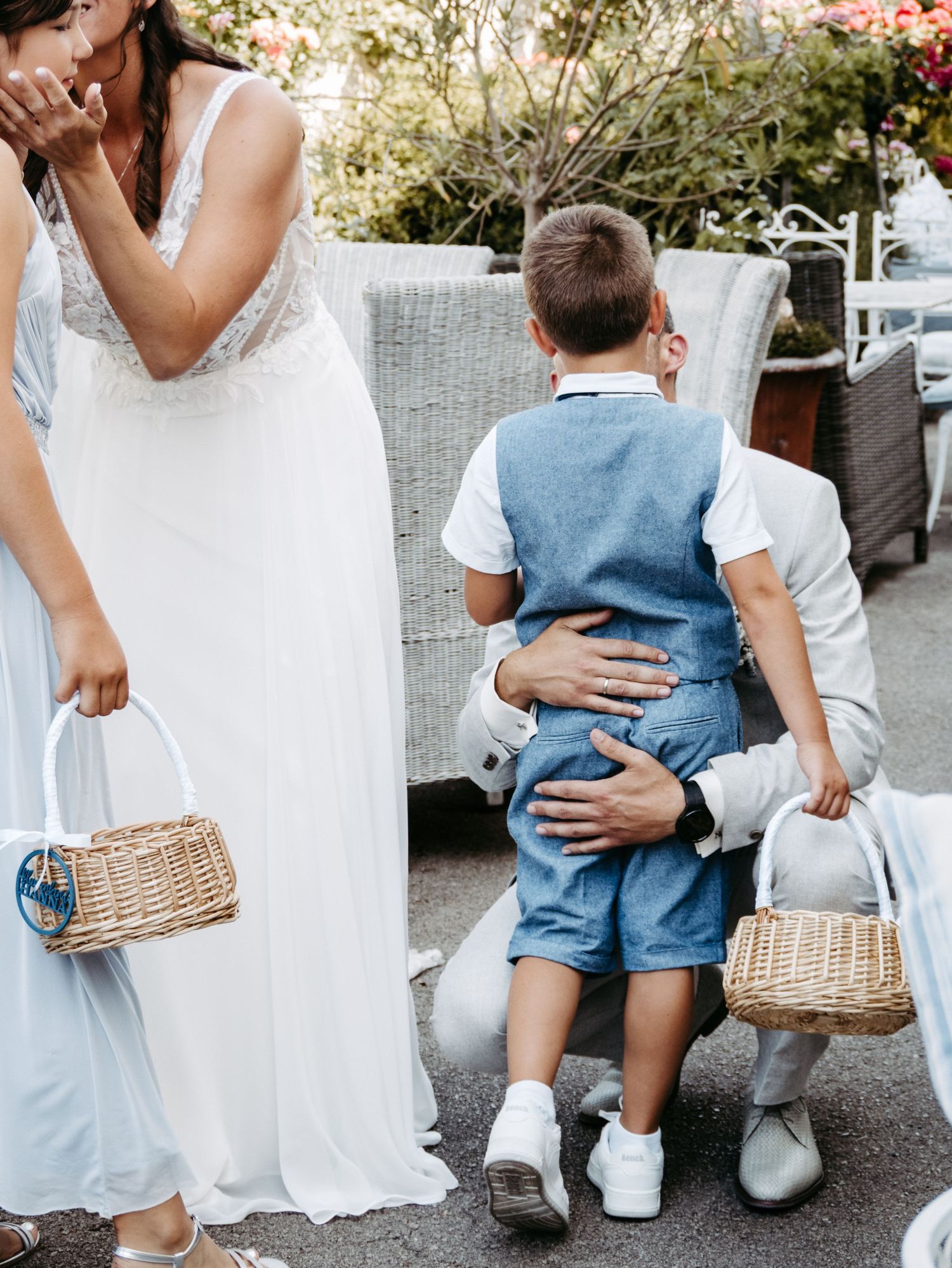 Wedding scene with bride in white lace gown hugging a boy in blue overalls, flanked by children holding wicker baskets.