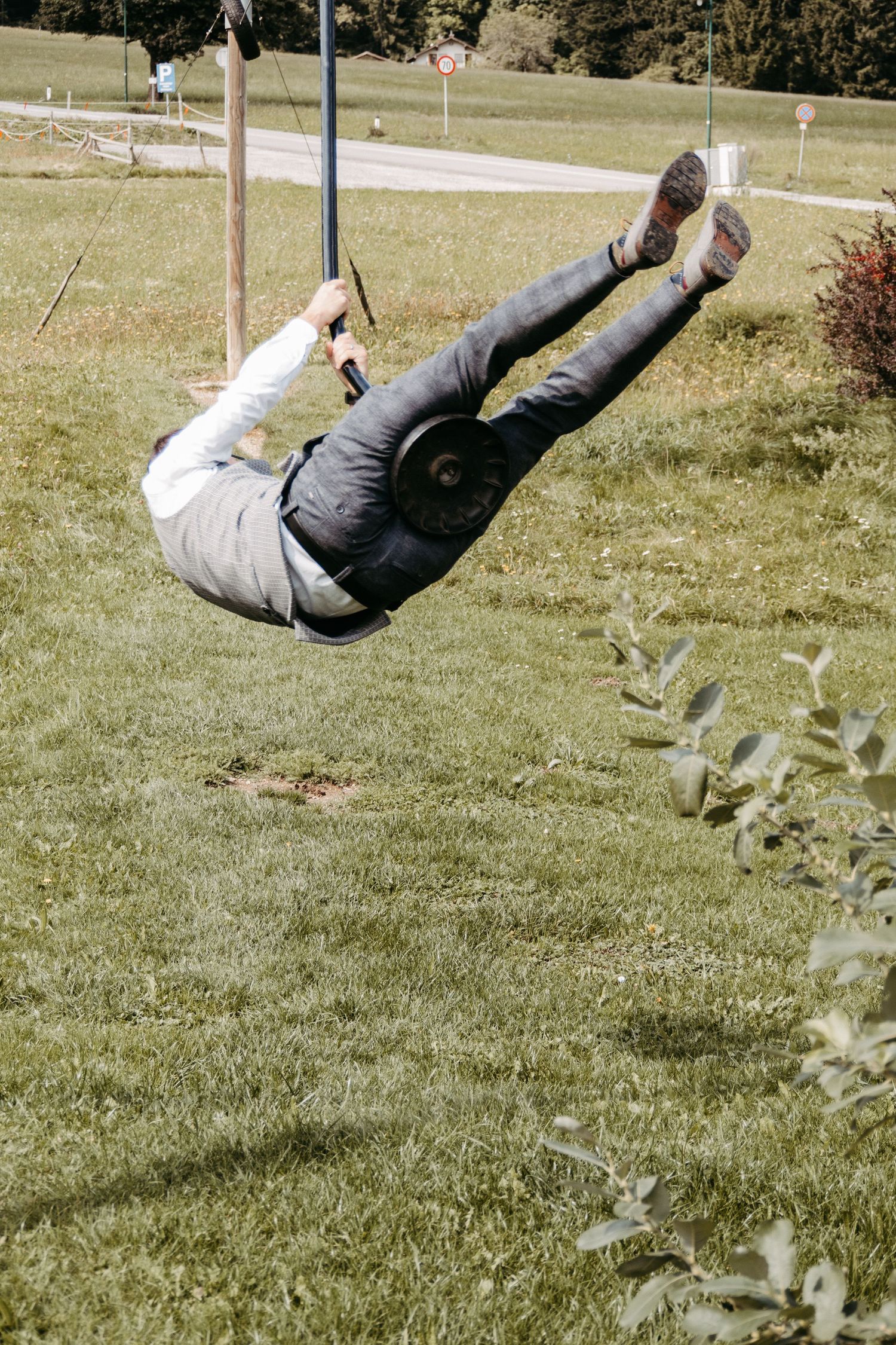 Person swinging on a rope over a lush green grass field outdoors on a sunny day.