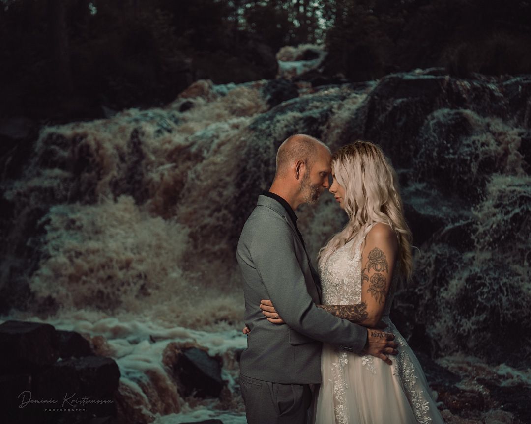 A romantic couple shares intimate moments in a moody forest setting with dark dramatic lighting and natural scenery.