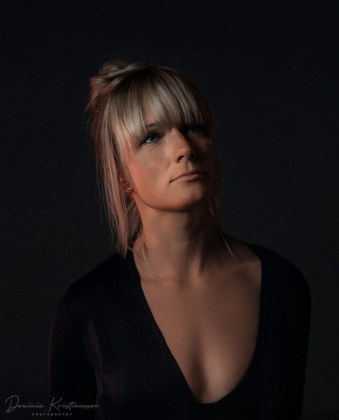 Dramatic low-key portrait against a black background with moody lighting.