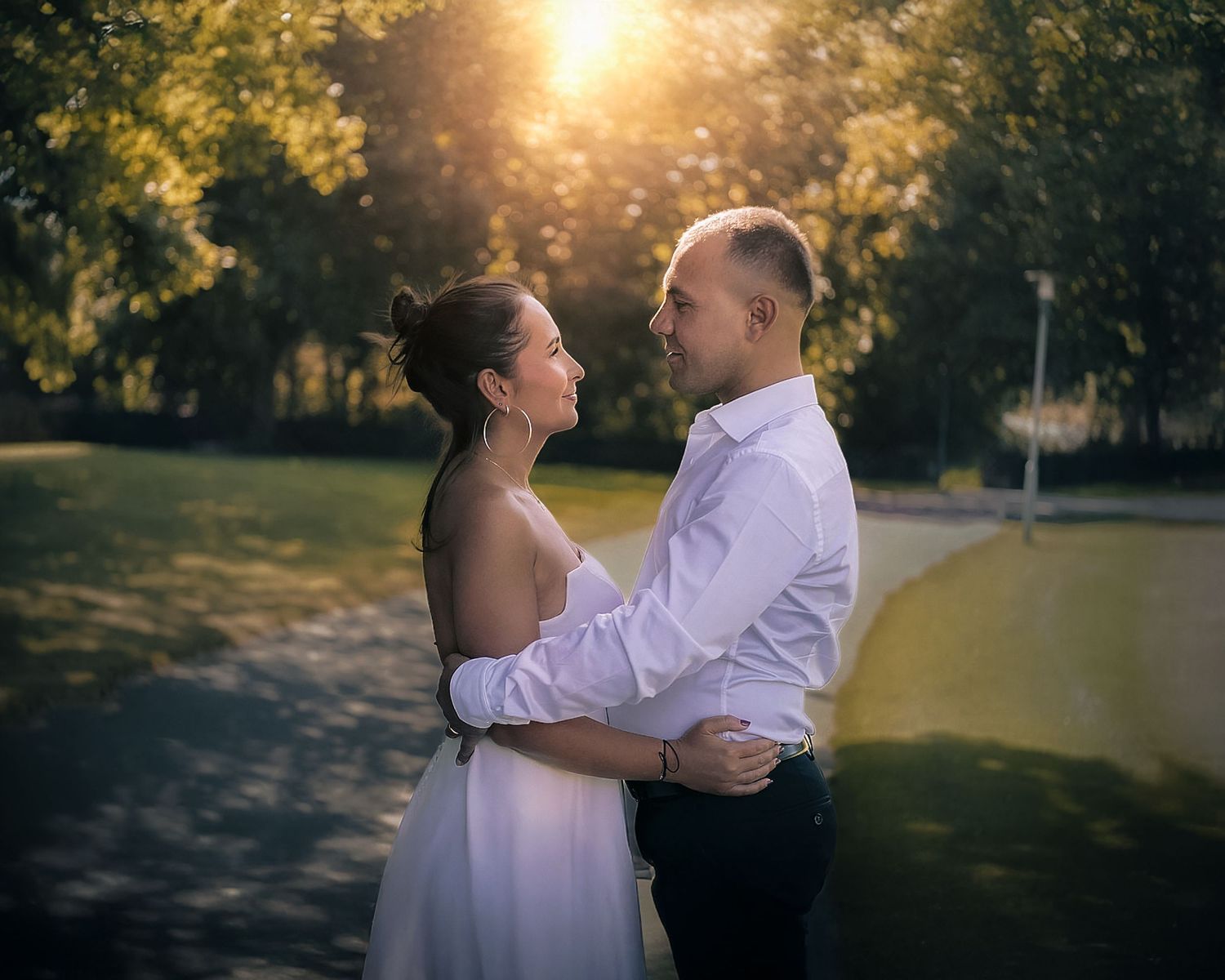 A romantic couple dances together in a park during golden hour with sunlight streaming through autumn trees.
