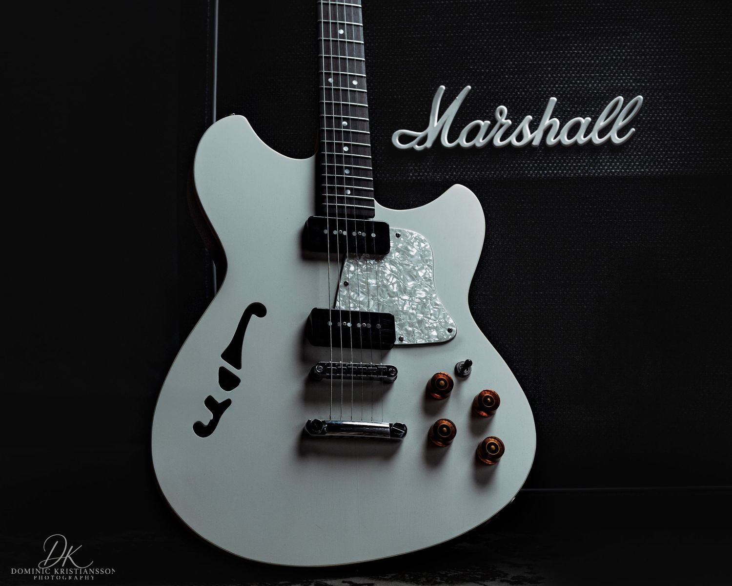 White semi-hollow electric guitar with chrome hardware positioned against a black Marshall amplifier background.