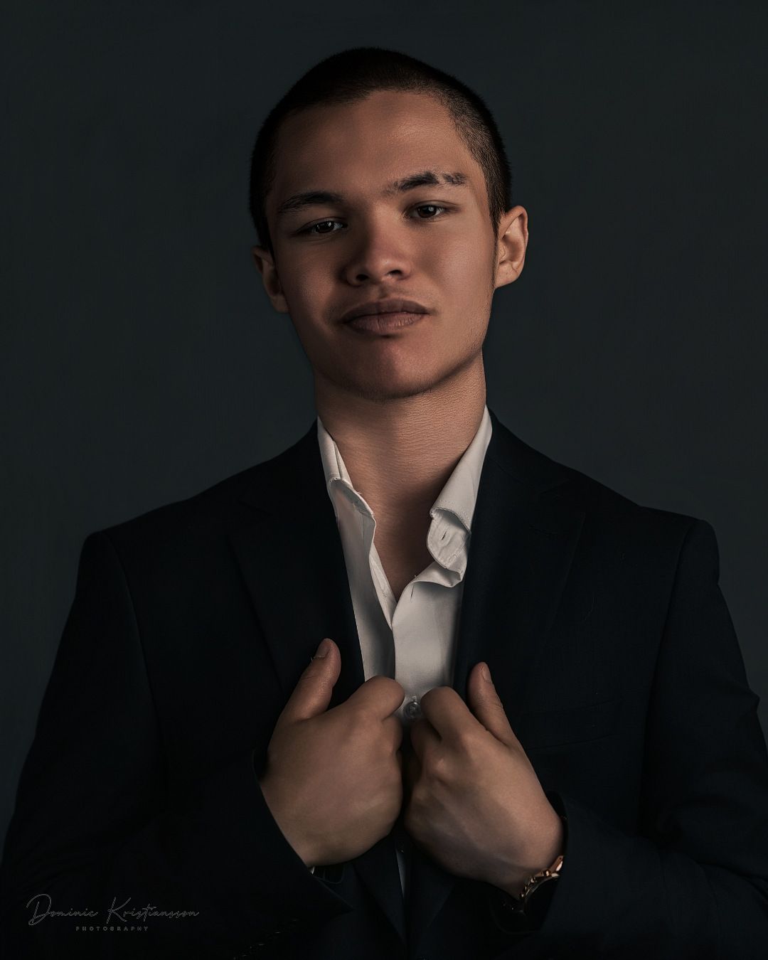 A professional studio portrait in formal attire against a dark background.