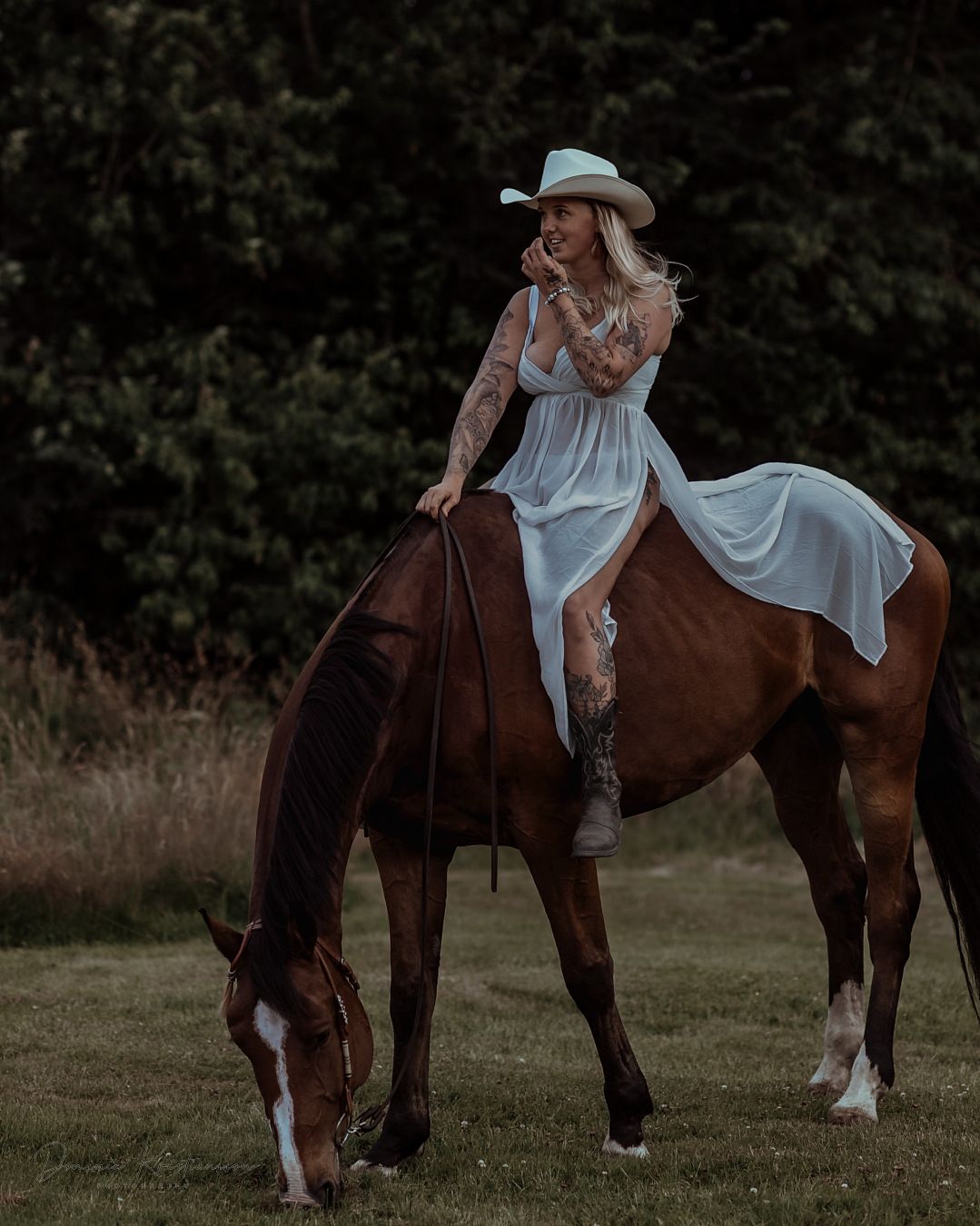 A moody photo series of a woman in a flowing white dress sitting side-saddle on a brown horse in a field at dusk.