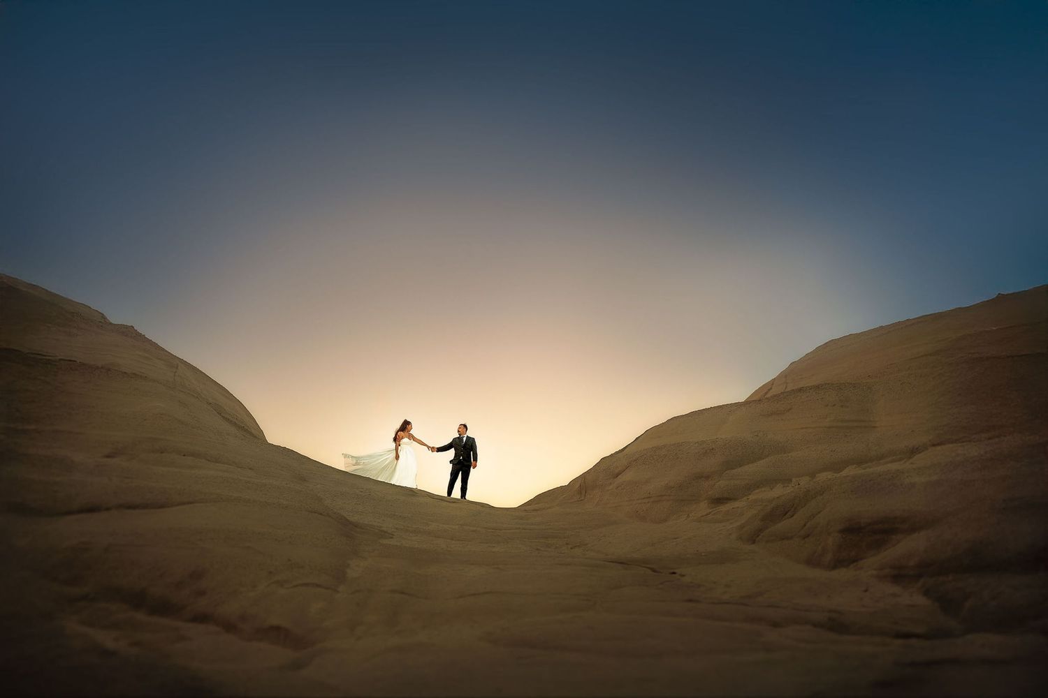 Two silhouettes standing on a desert ridge at golden hour.