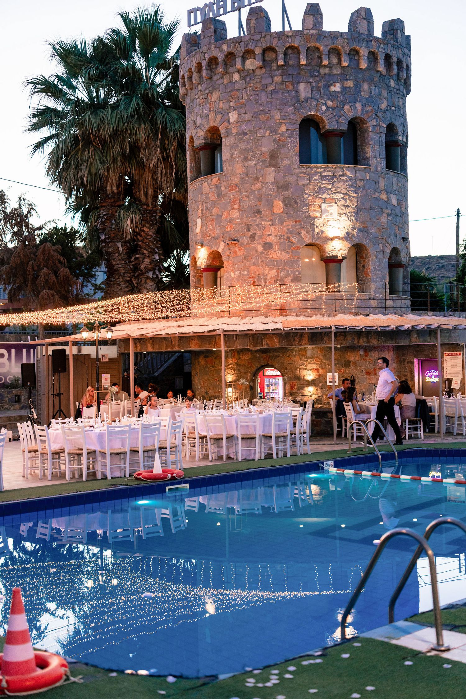 Elegant poolside wedding venue with castle-like architecture and string lights at dusk.