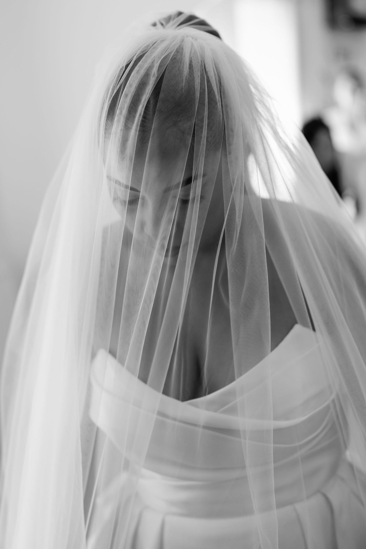 Ethereal side view of a bride wearing a flowing white veil against a light background.