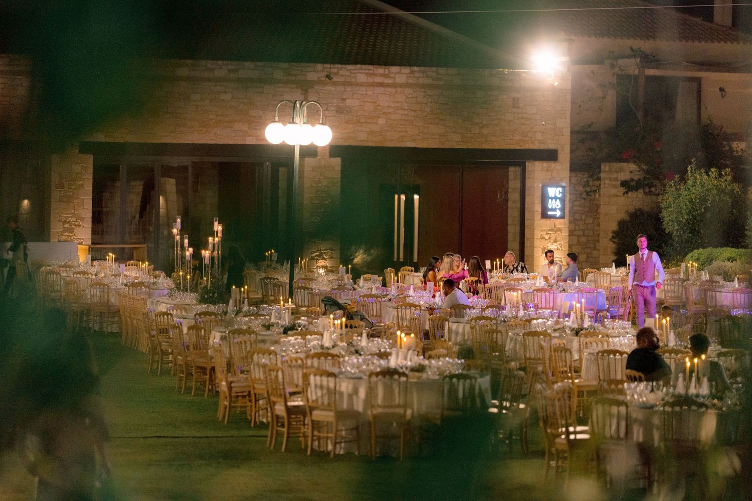 Elegant outdoor wedding reception venue illuminated at night with warm lighting and wooden chairs.