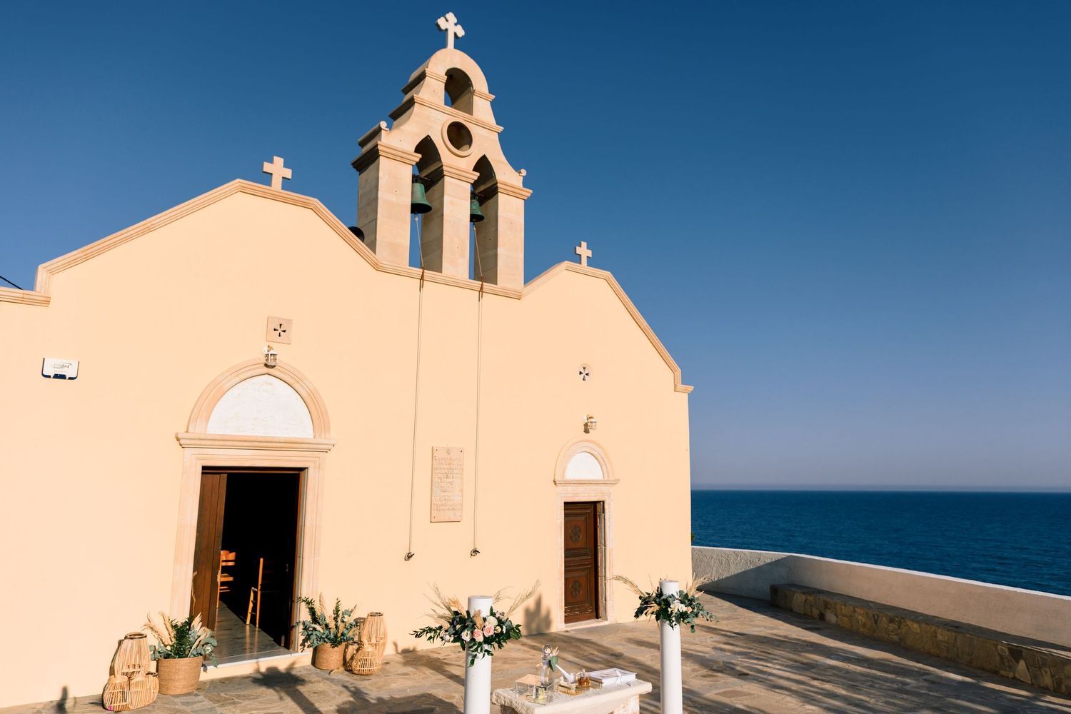 Traditional white Mediterranean church with bell tower against bright blue ocean backdrop.