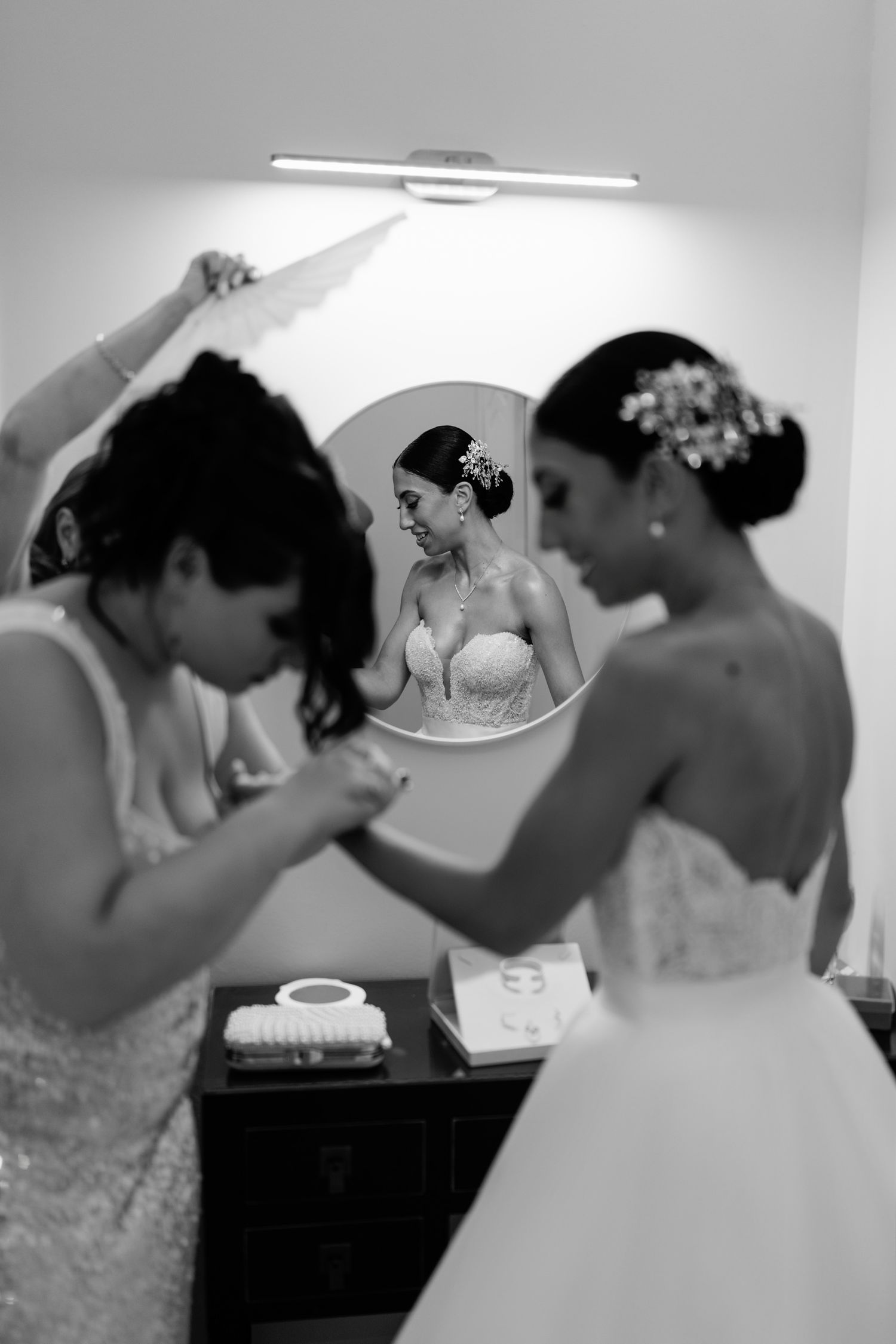 Bridesmaids in matching dresses prepare in a dressing room with mirrors.