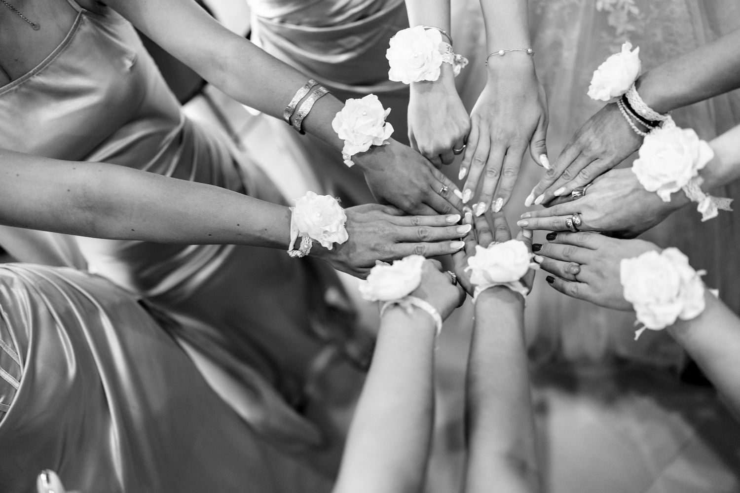 Black and white image of hands joined in a circle holding white roses.