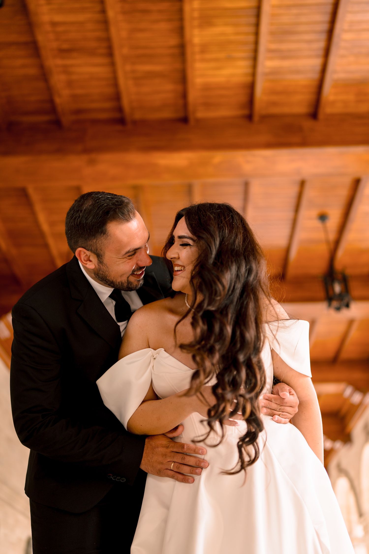 Romantic moment captured under wooden beams in warm lighting.
