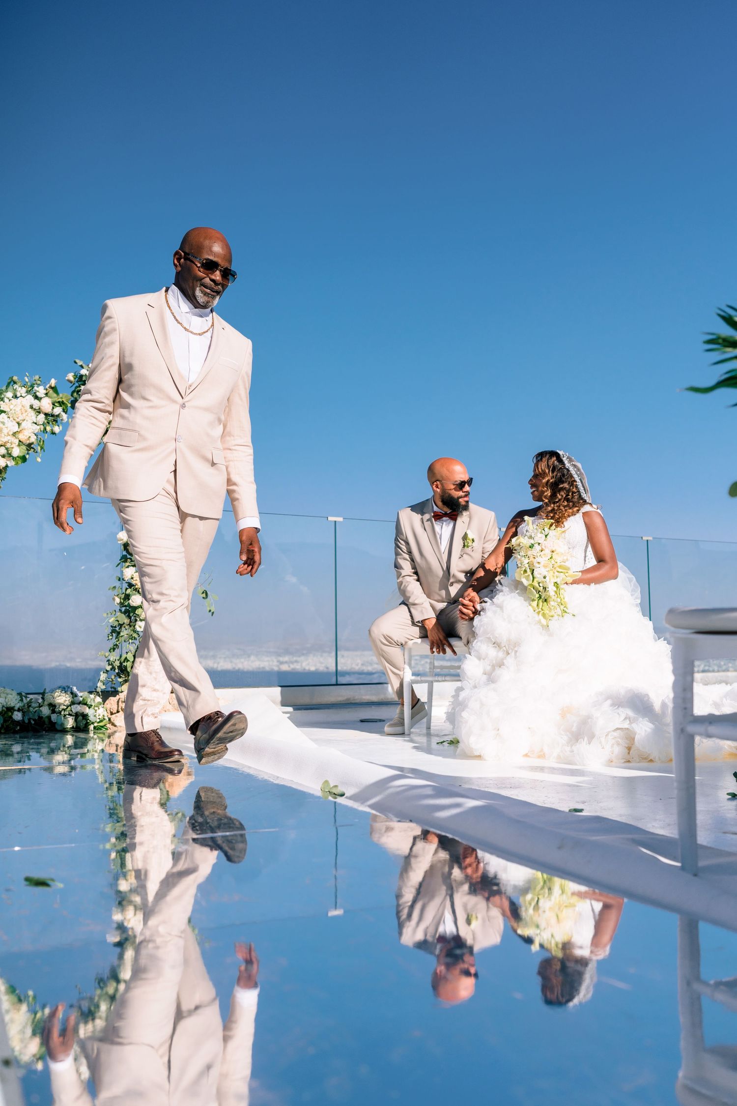 Wedding couple shares a romantic moment on a reflective surface with blue sky backdrop.