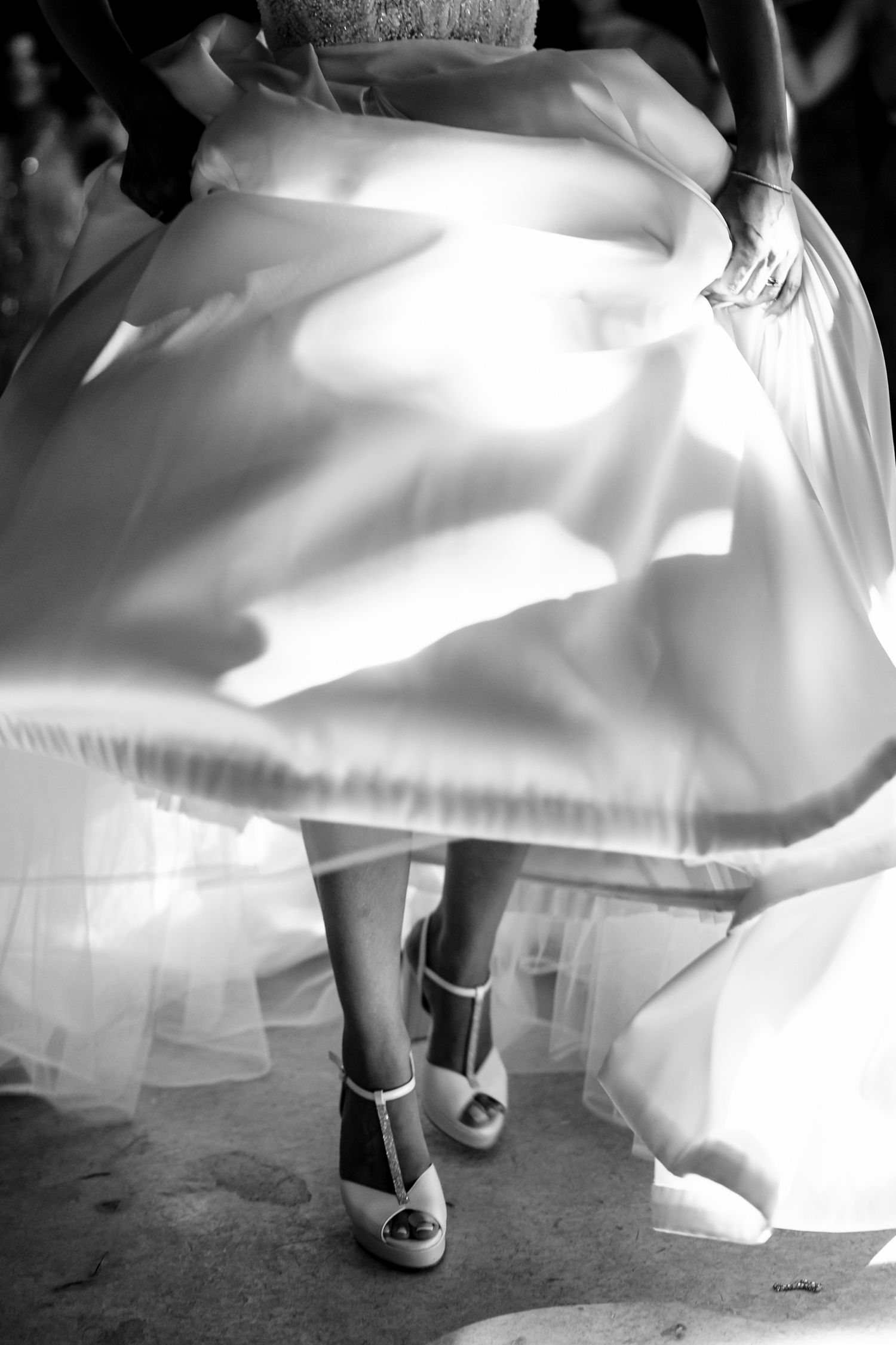Close-up of a white wedding dress swirling in motion with peep-toe shoes visible.