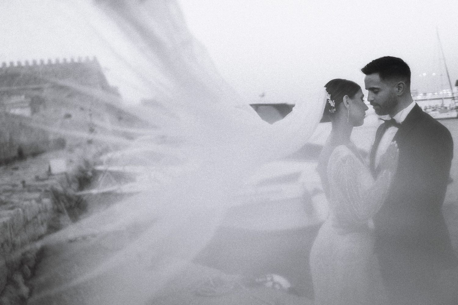 A romantic black and white wedding photo with a flowing veil creating an ethereal effect.