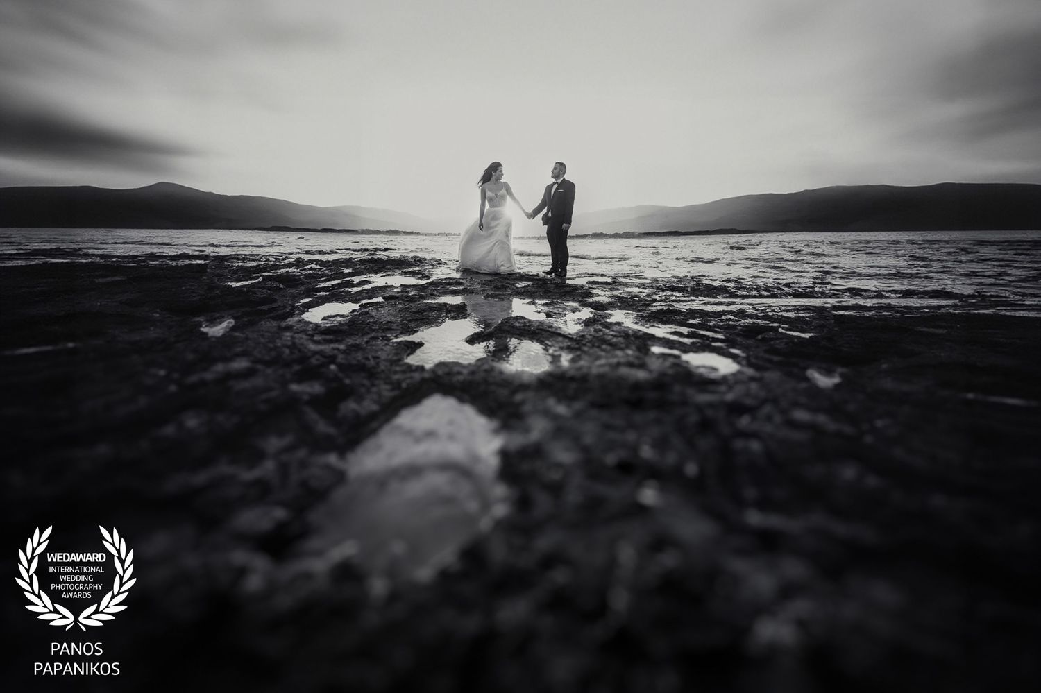 Black and white panoramic landscape with silhouettes against dramatic sky.