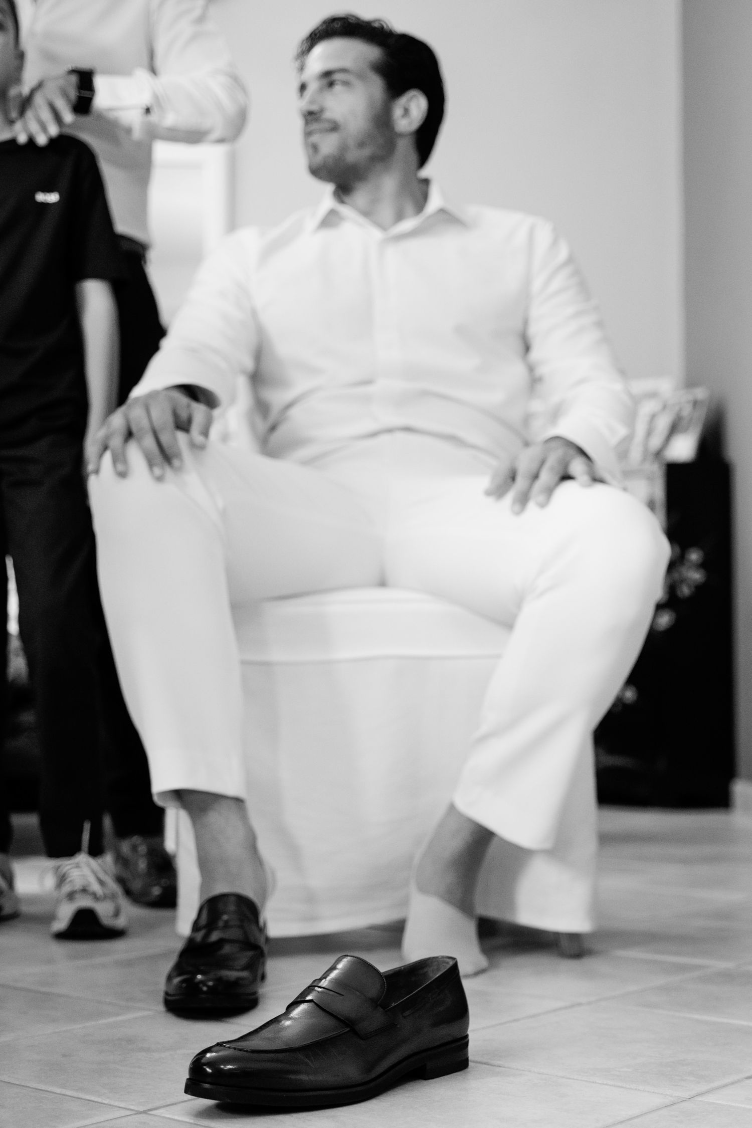 Black and white photo shows formal shoes and white pants during wedding preparations.