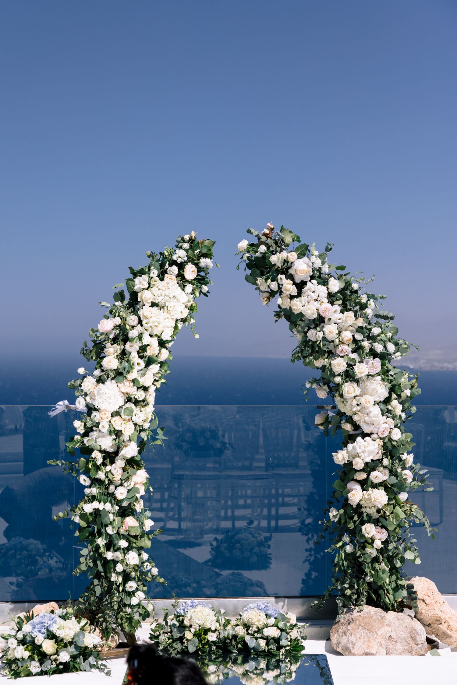 White floral arch arrangements against blue ocean backdrop for wedding ceremony.