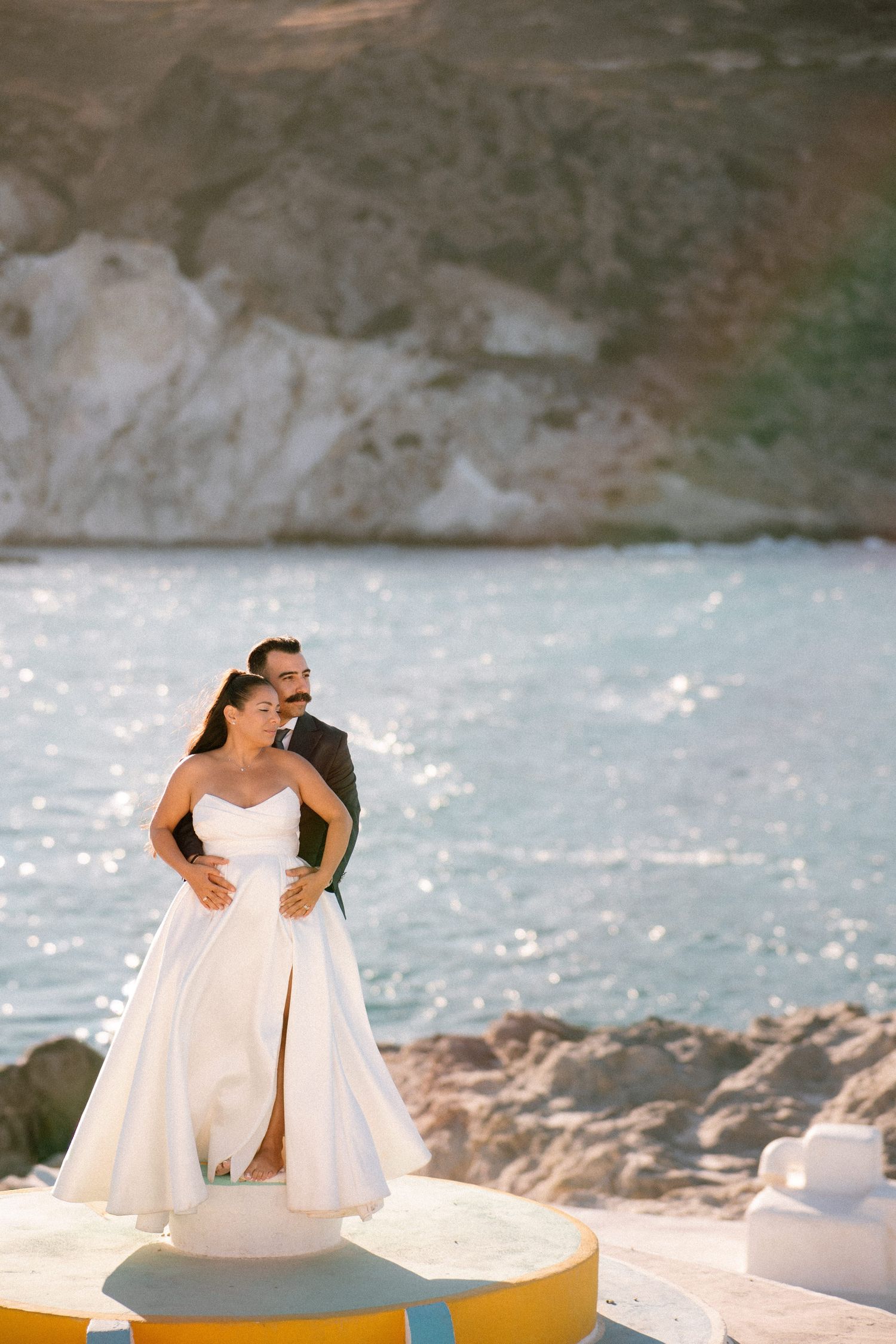 A flowing white wedding dress billows in the wind against a coastal backdrop.