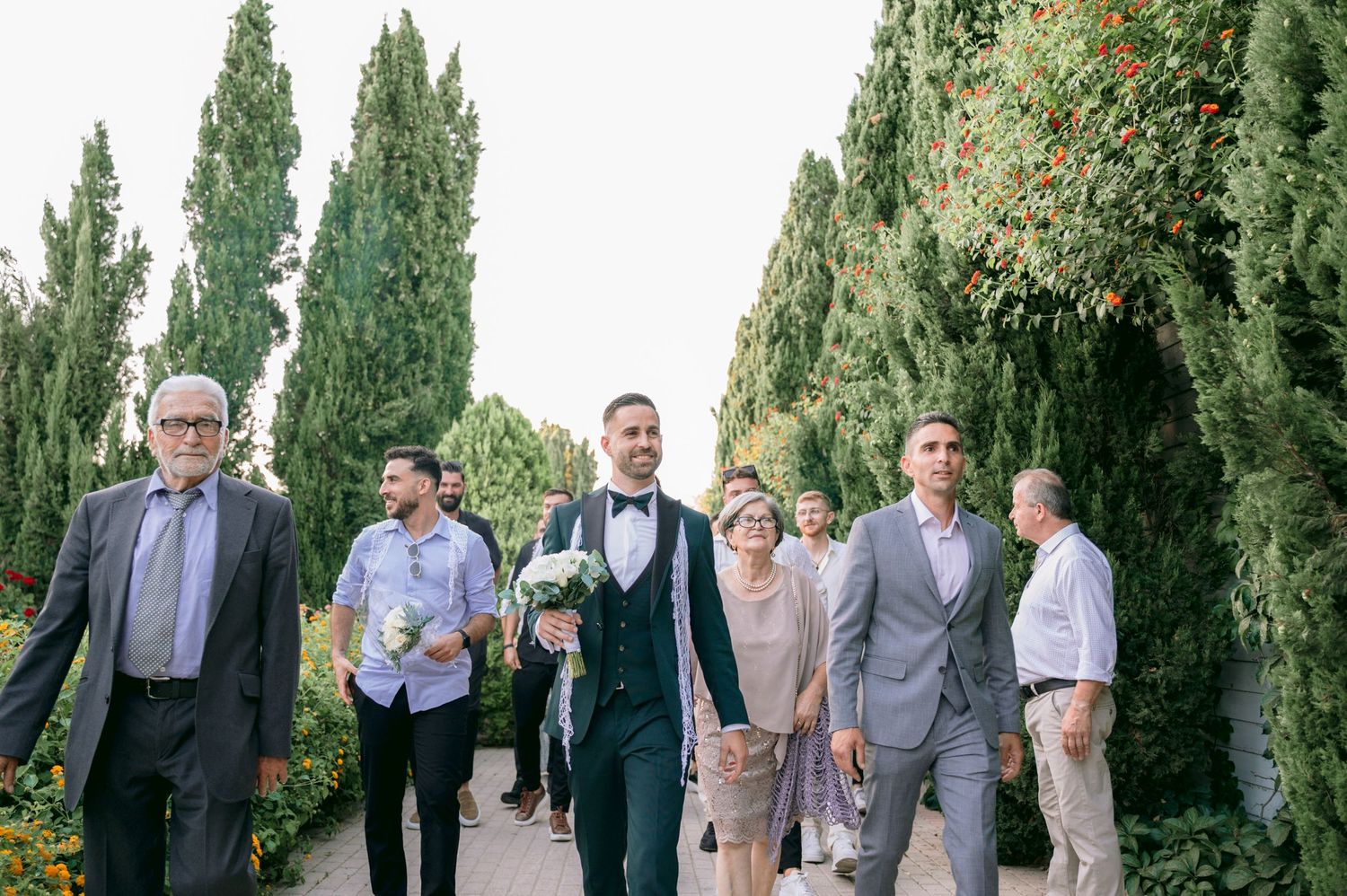 Wedding party poses together outdoors with tall cypress trees in background.