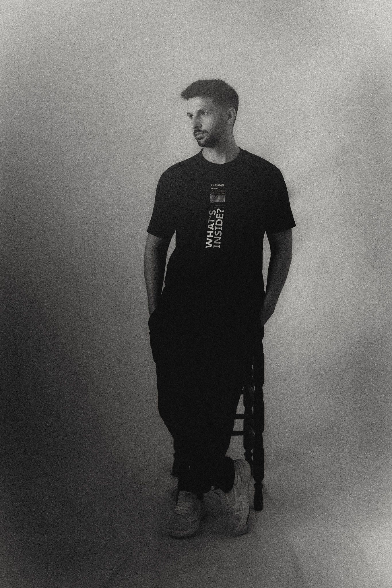 Person in black t-shirt poses against grey background in artistic portrait series.
