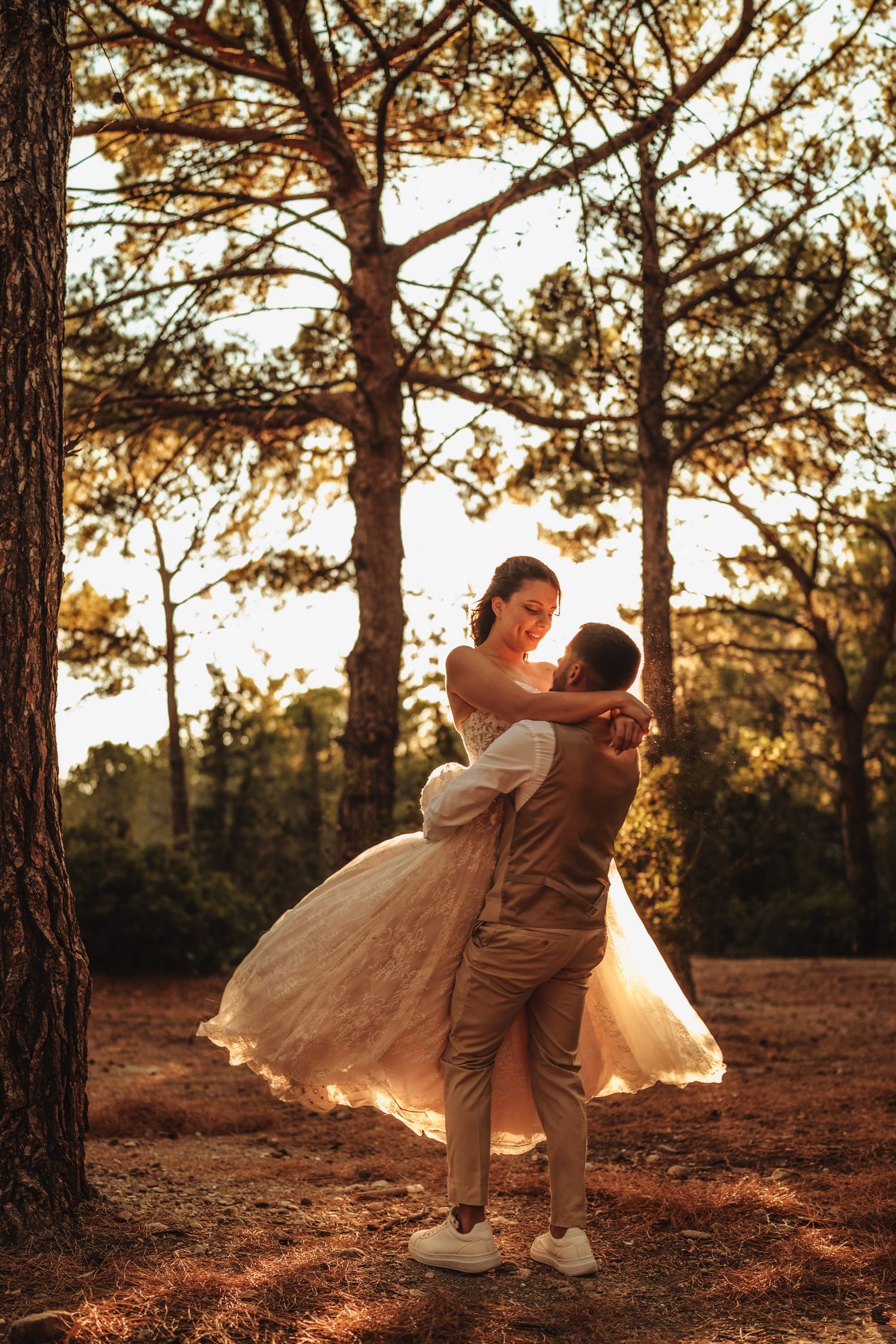 A couple dances playfully among pine trees during sunset.