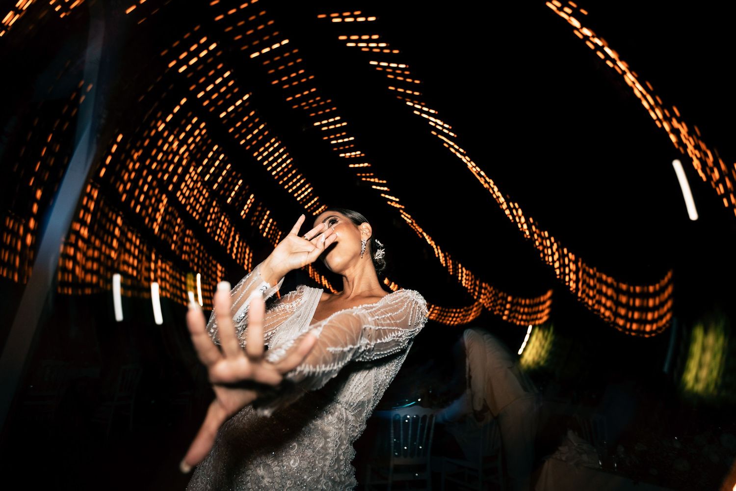 Dynamic dance moves captured under romantic string light canopy at wedding reception.