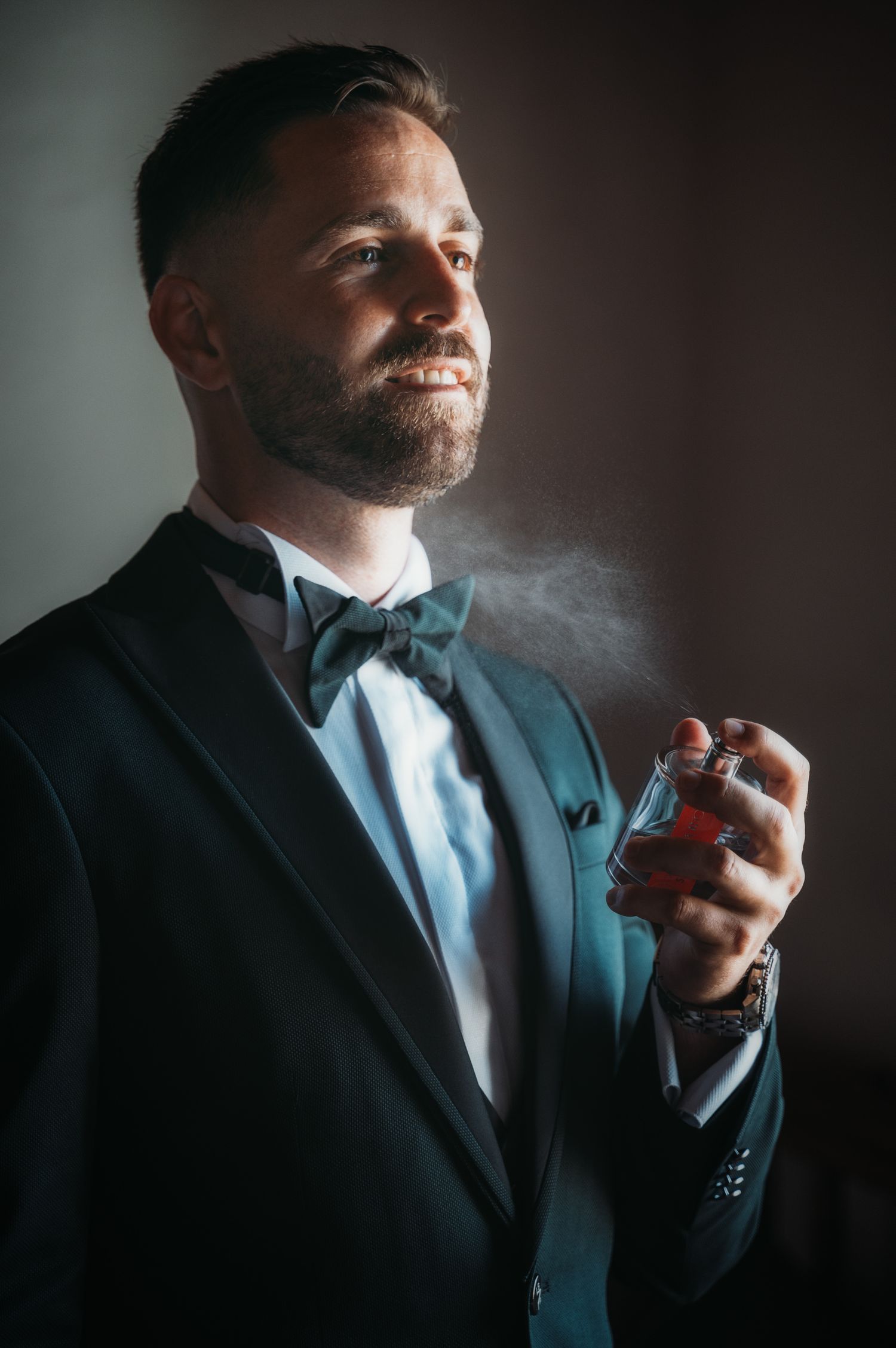 Dramatic lighting captures someone in a tuxedo spraying cologne in a getting-ready sequence.
