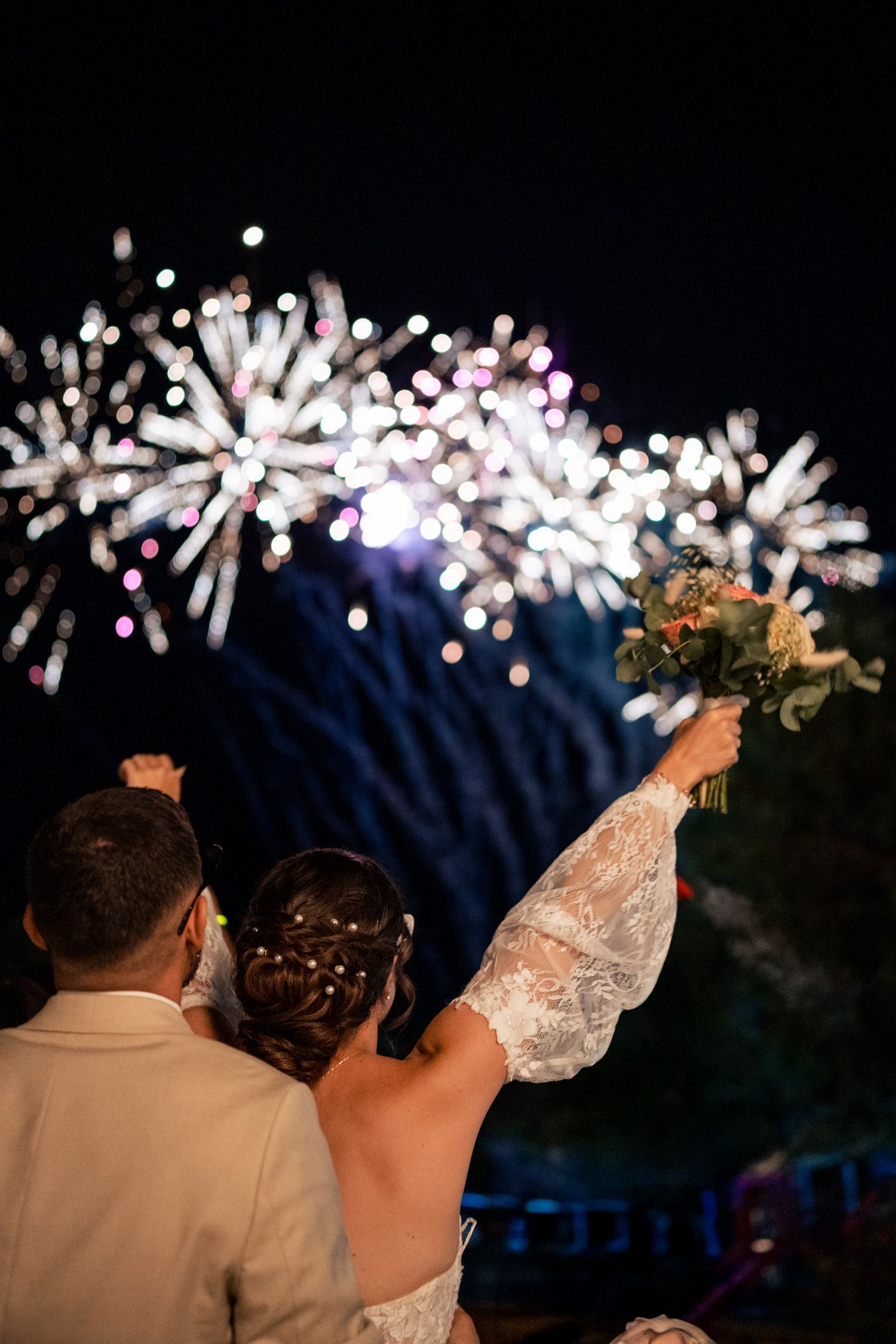 Wedding guests watching fireworks display against dark night sky.