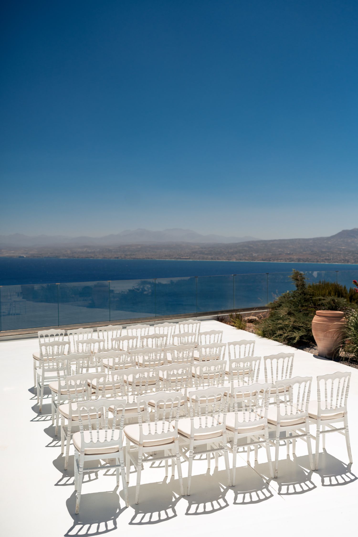 White wedding chairs arranged in rows overlooking a scenic ocean and mountain view.