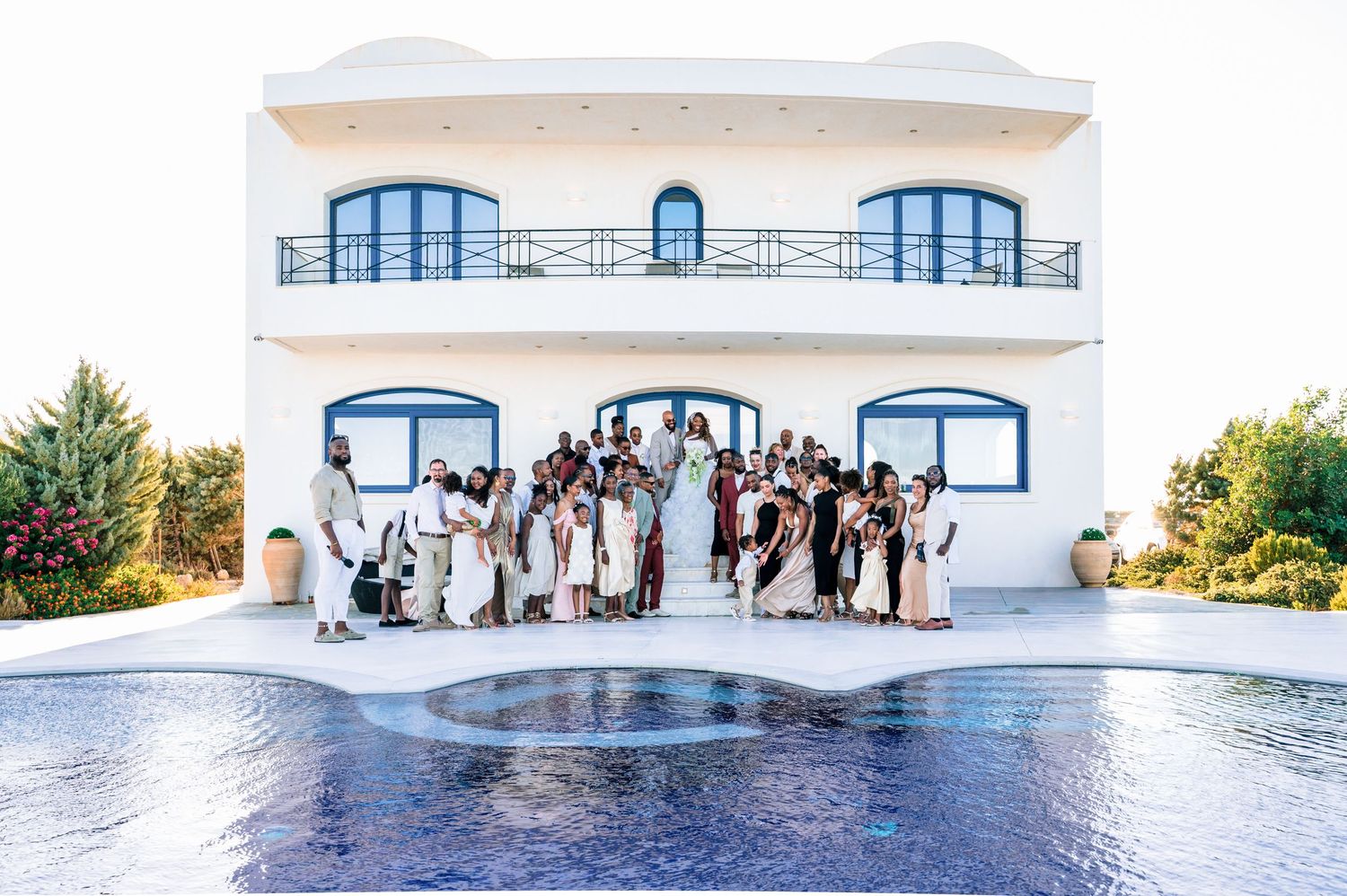 Panoramic view of white Mediterranean-style building with blue accents and wedding guests.