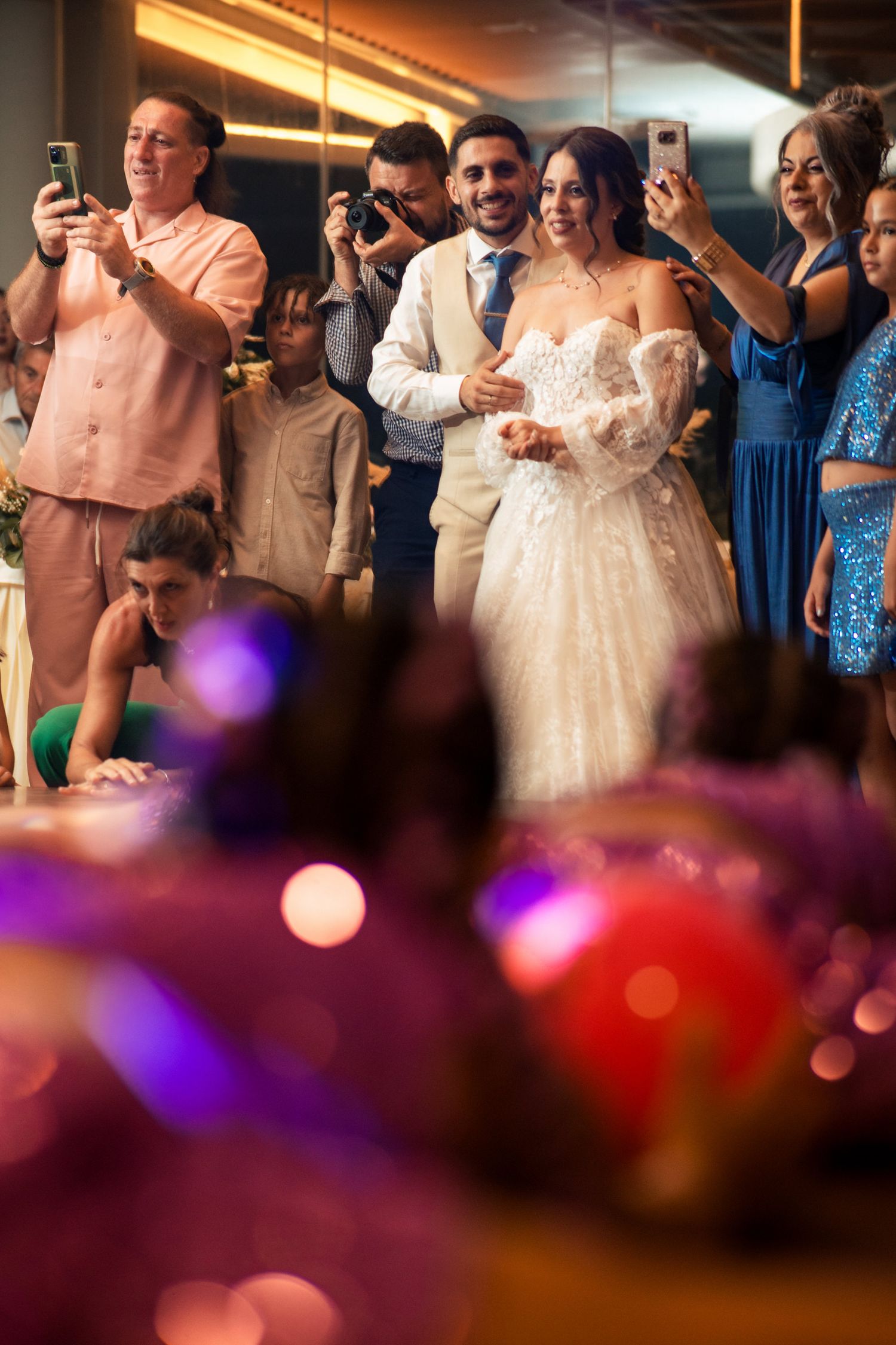 Wedding reception crowd watches dance floor with colorful purple and red bokeh lights in foreground.