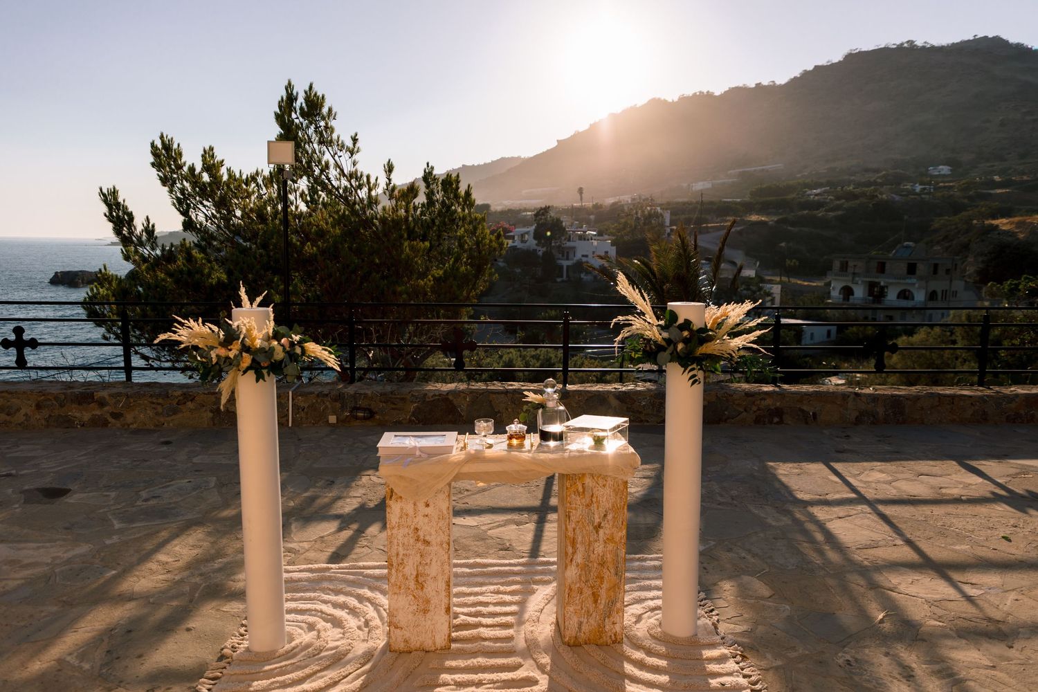 Elegant outdoor wedding venue with white pillars and floral arrangements against a mountainous backdrop at sunset.