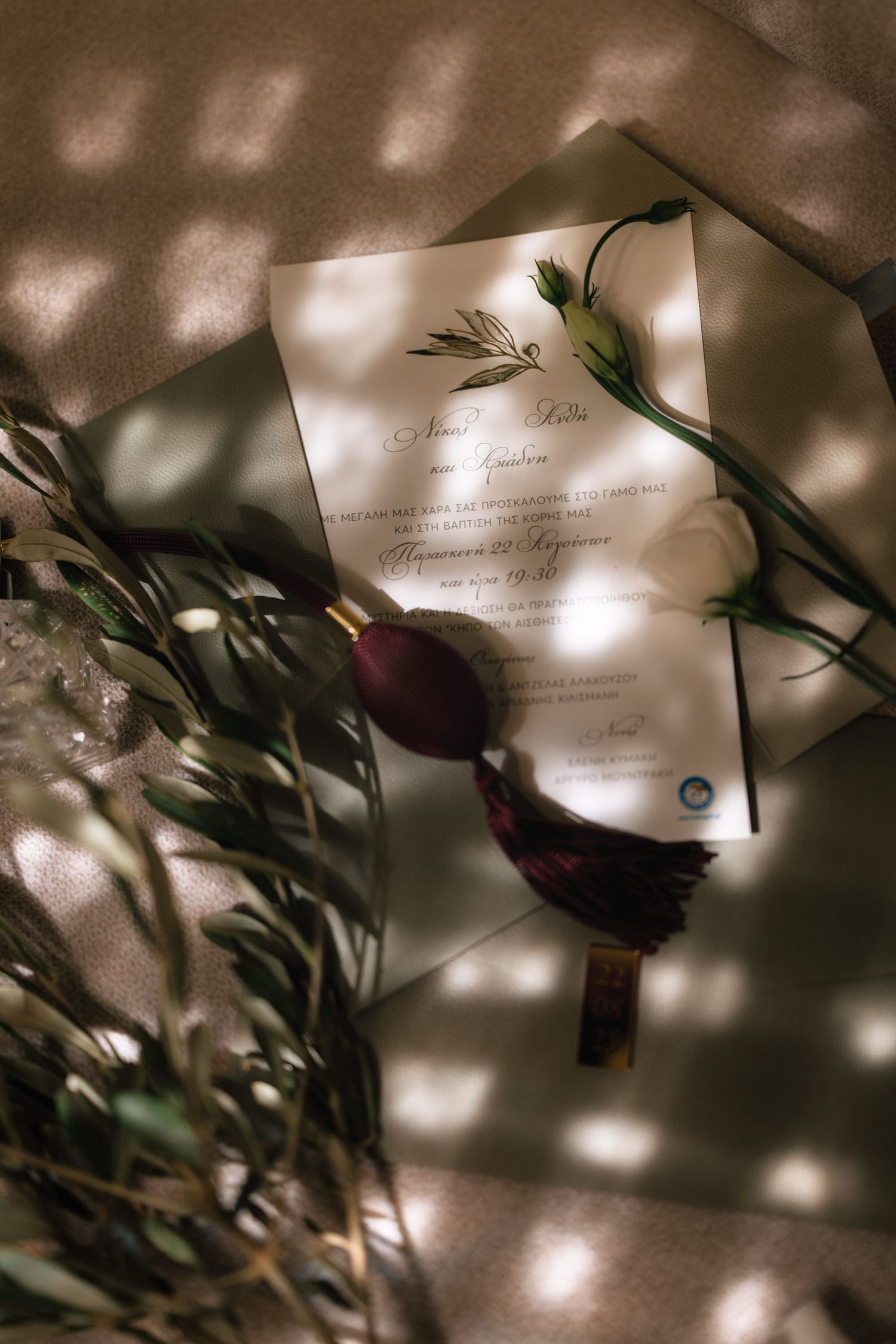 Artistic detail shot of wedding invitation with soft bokeh lighting and green foliage.