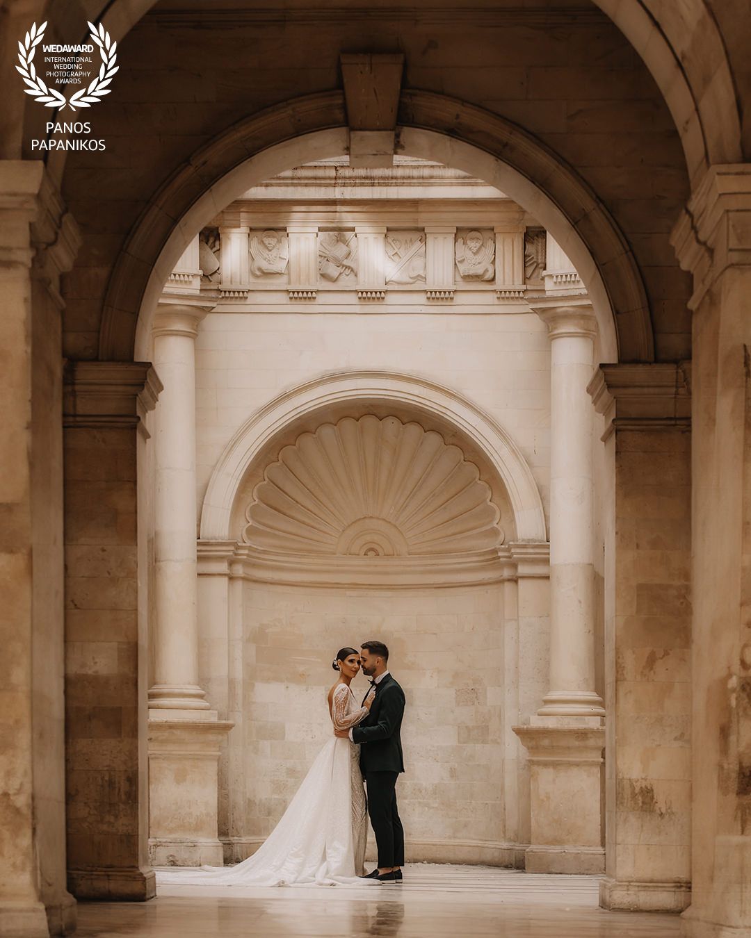 Wedding couple in romantic poses against classical stone architecture with arched details.