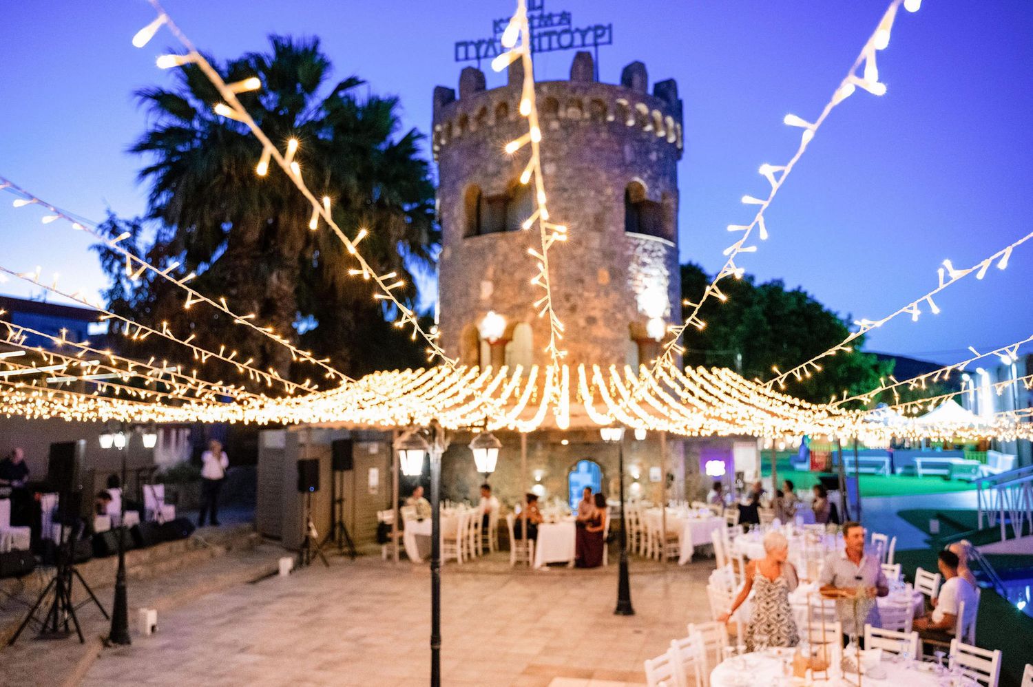 String lights illuminating an outdoor wedding venue at twilight with castle architecture.